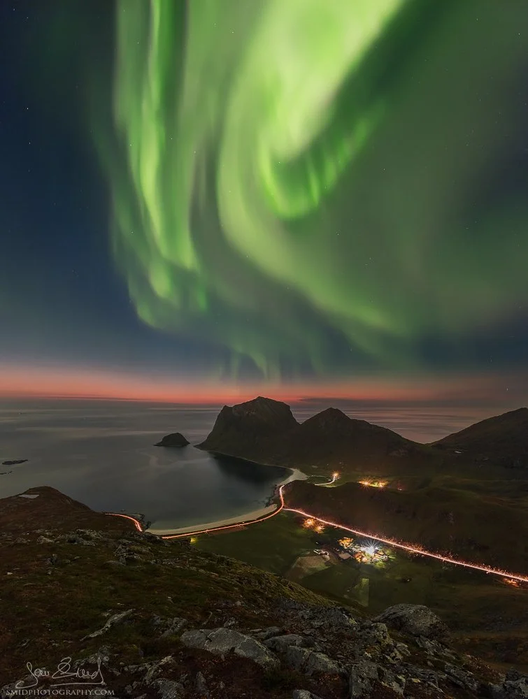 Vertical panoramic photograph "Sunset in a Green Robe" capturing a rare combination of a post-sunset glow and Aurora Borealis over a hidden Lofoten bay. Captured by Jan Smid, Master QEP, in 2017.