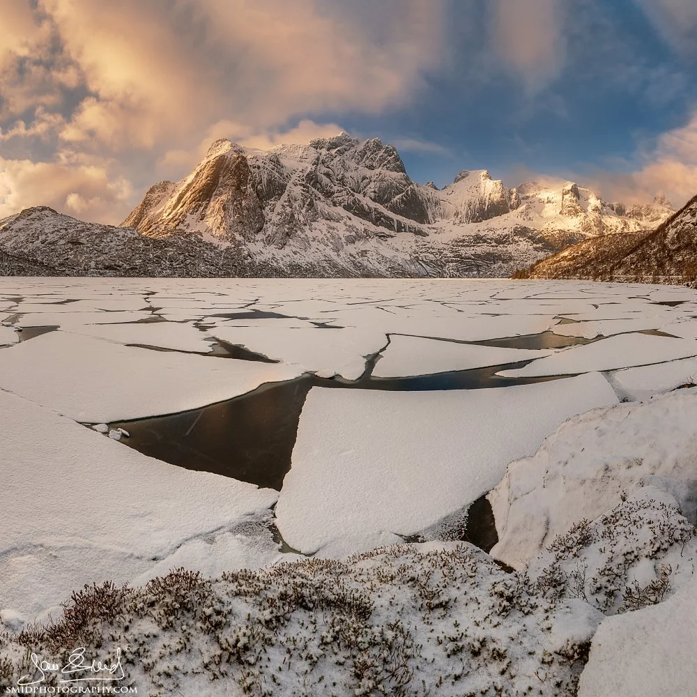 Panoramic photograph "Ice Floes" showing cracked ice on a frozen arctic lake with snow-capped mountains in the background. Captured by Jan Smid, Master QEP, in 2019.