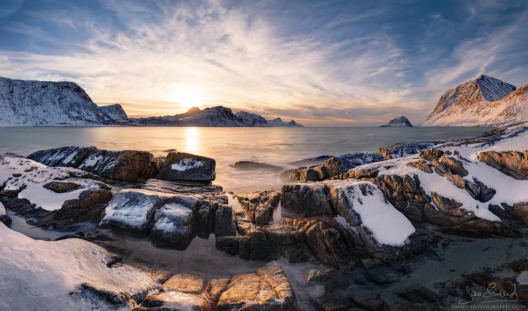 Panoramic winter landscape photograph "Stone Path to the Sea" featuring snow-covered rocks and golden arctic light on Vik Beach, Lofoten. Captured by Jan Smid, Master QEP, in 2022.
