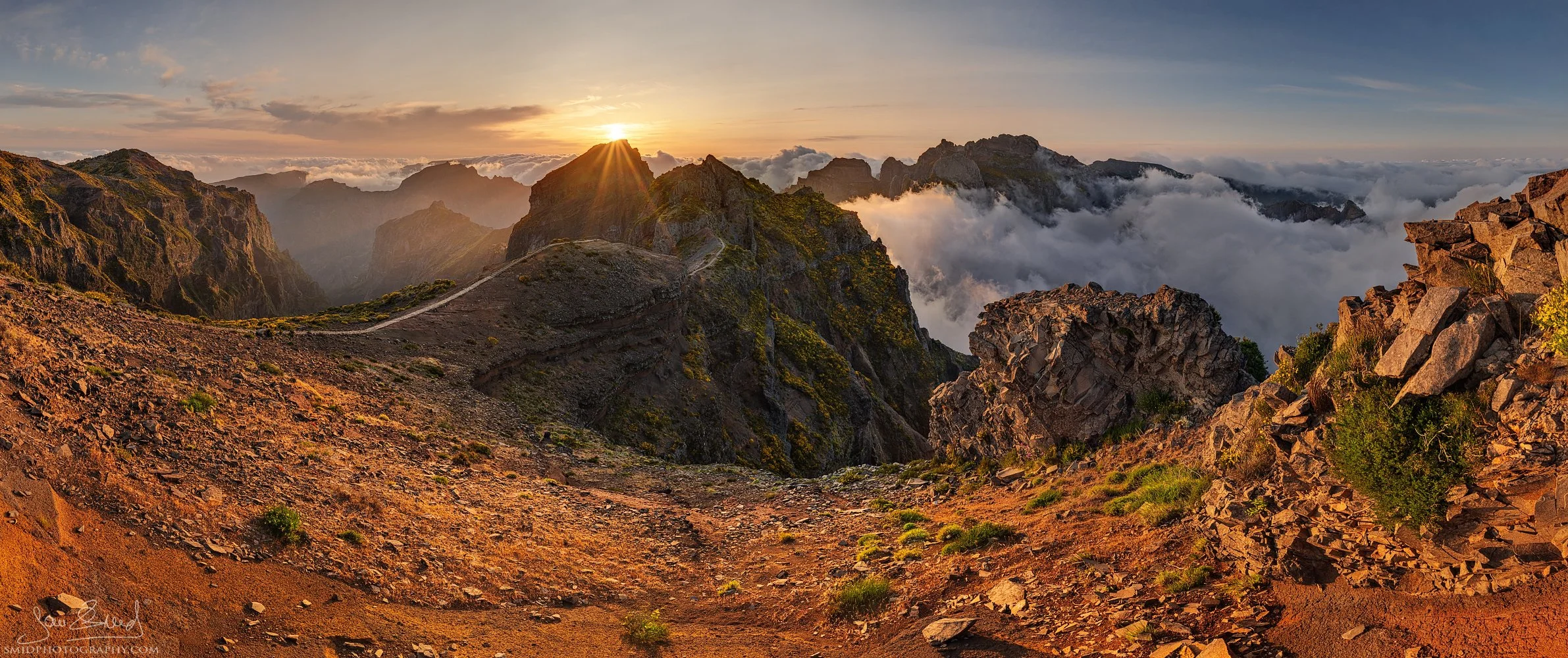 Panoramic landscape photograph "In a Cloudy Sea" capturing the dramatic peaks of Pico do Arieiro, Madeira, rising above a vast sea of clouds during a golden sunset. Captured by Jan Smid, Master QEP, during a 2023 photography expedition.