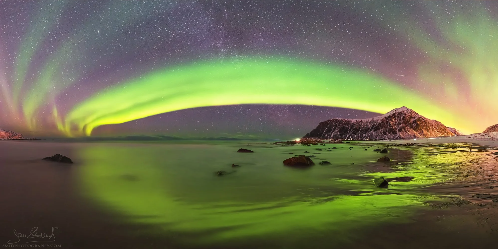 Award-winning panoramic photograph "Green Tide" capturing a vibrant Aurora Borealis reflecting in the coastal waves of the Lofoten Islands. Captured by Jan Smid, Master QEP, in 2019.