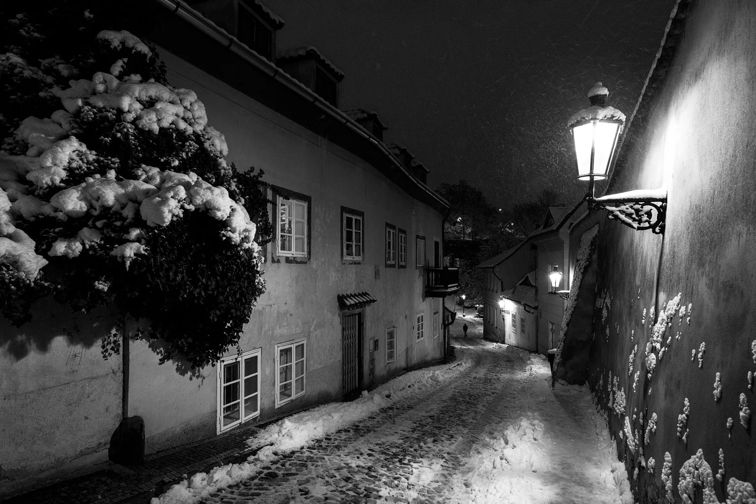 Atmospheric fine art photography titled "Lonely Walker." A solitary figure walking through the snow-covered streets of Nový Svět, Prague. Captured by Jan Smid, Master QEP, in 2019. Winter solitude in Hradčany.