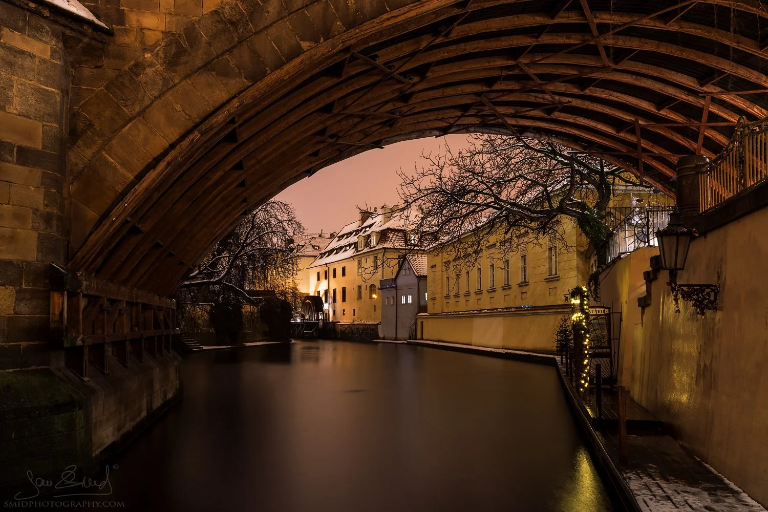 Award-winning fine art photography titled "In the Kingdom of Water Goblin." A mystical morning view under the Charles Bridge in Prague with heavy fog and the Vltava river. Captured by Jan Smid, Master QEP, in 2019.