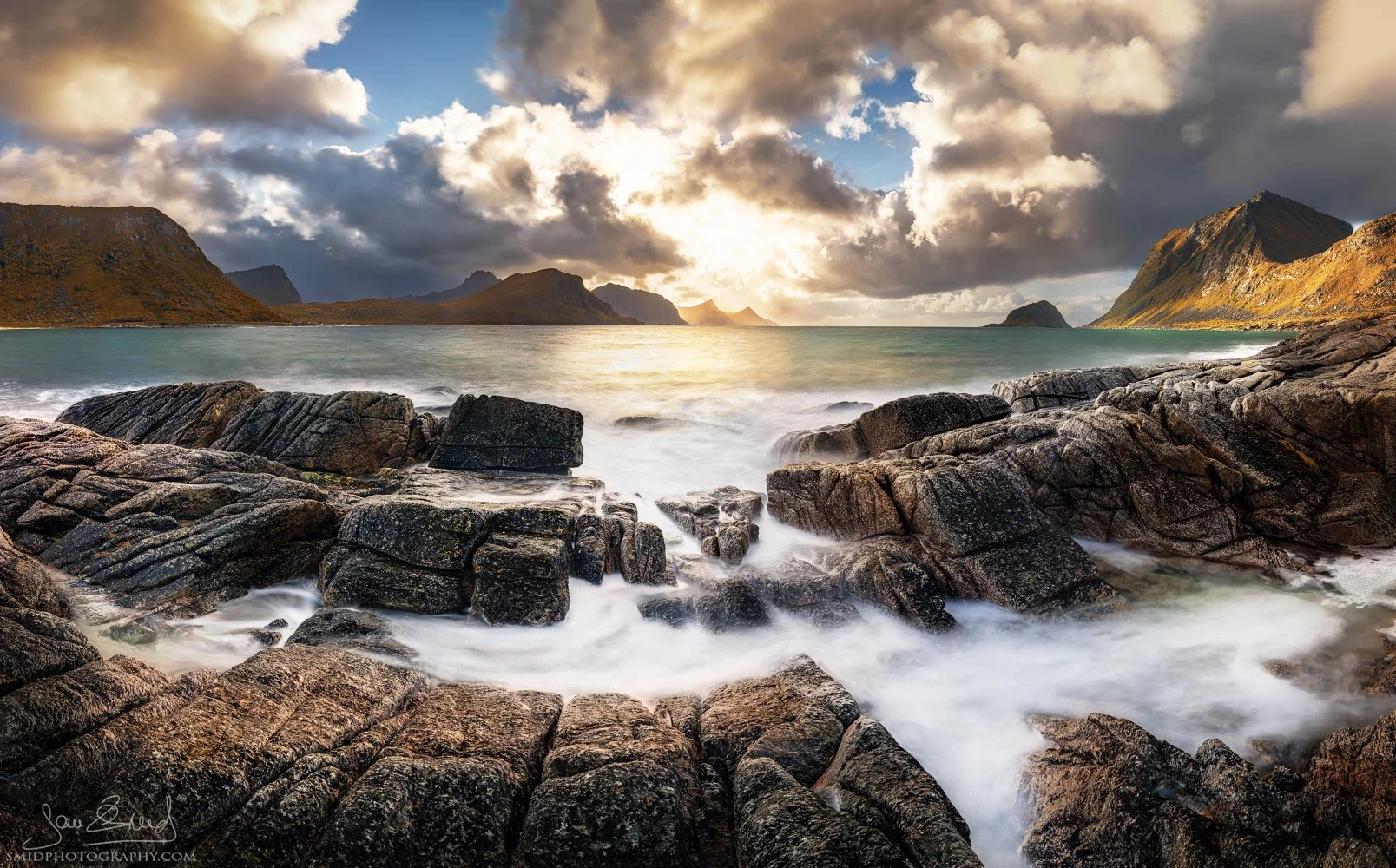 Masterful autumn panoramic view next to Haukland Beach, Lofoten, featuring the identical composition of the winter coastline with golden grasses, colorful foliage on peaks, and warm sunset light over the rocky shore, by Jan Smid Master QEP.