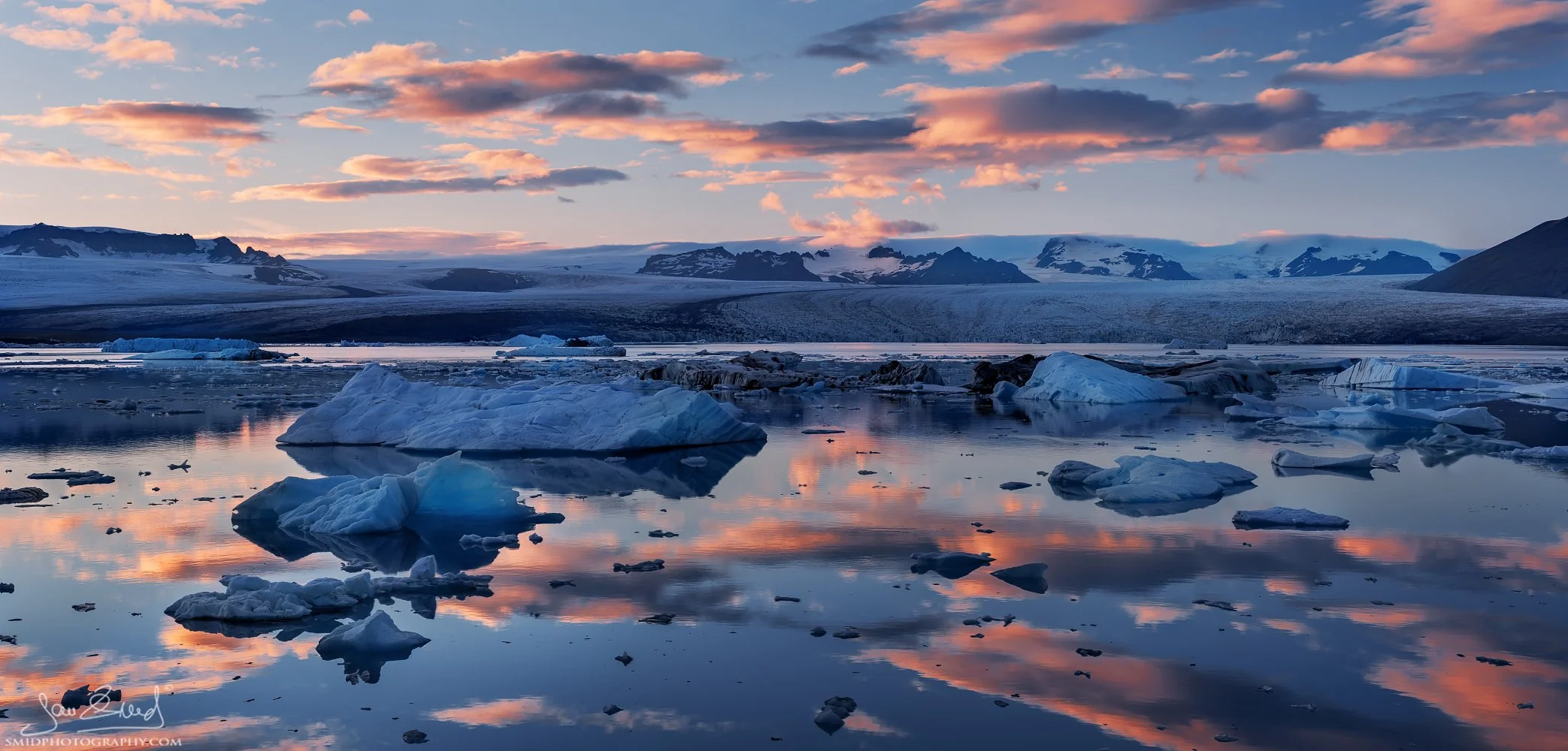 Fine art sunset panorama titled "Sunset Ice Drifts" at Jökulsárlón glacier lagoon, Iceland. Large icebergs drifting in the blue lagoon during Jan Smid’s 2015 photo expedition. Captured by Jan Smid, Master QEP. Dramatic Arctic landscape.