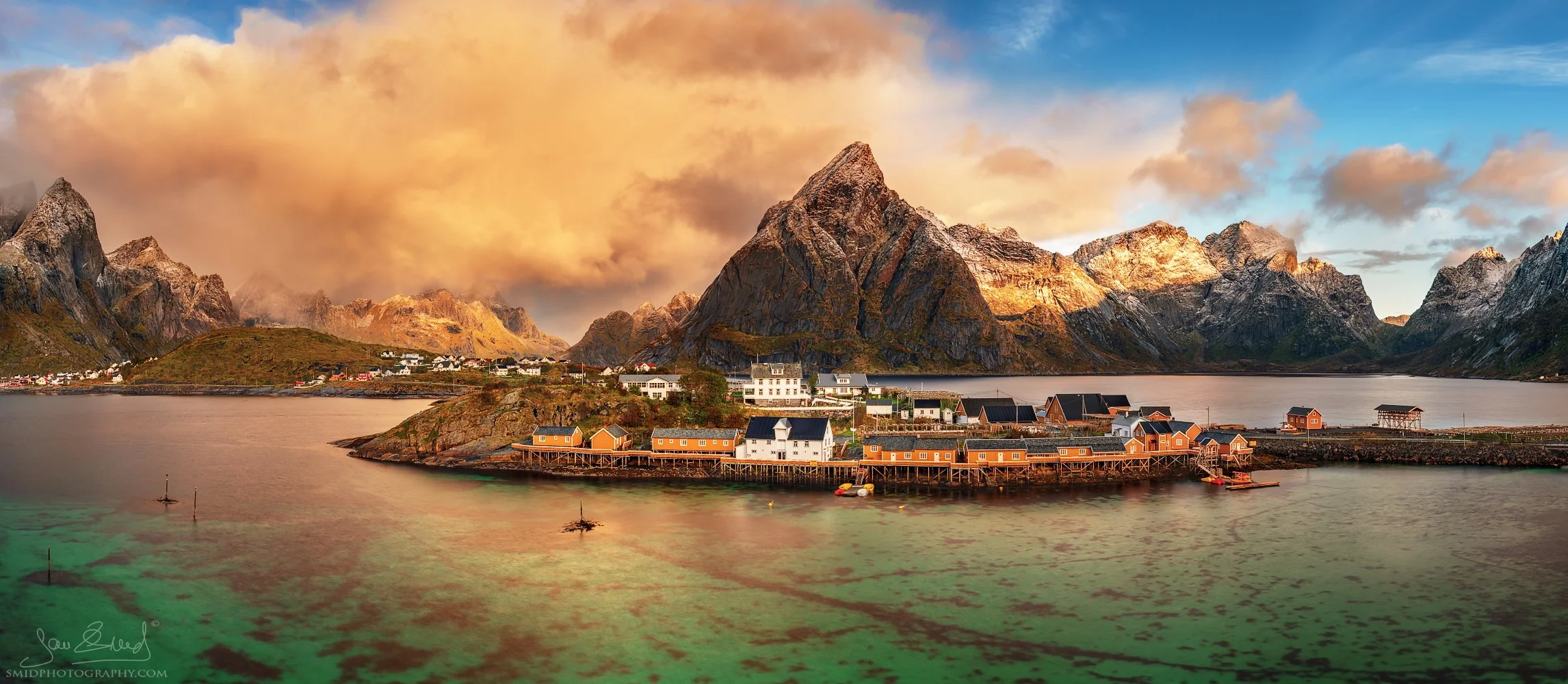 Award-winning panoramic photograph "A Power of Turquoise View" featuring the red cabins of Hamnøy nestled against a snow-capped mountain. Captured by Jan Smid, Master QEP, in 2018.