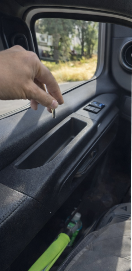 A person's hand reaching into a Mercedes-Benz sprinter interior door panel with MARV armrest installed in order to install a bolt, with the window showing trees and a yard outside.