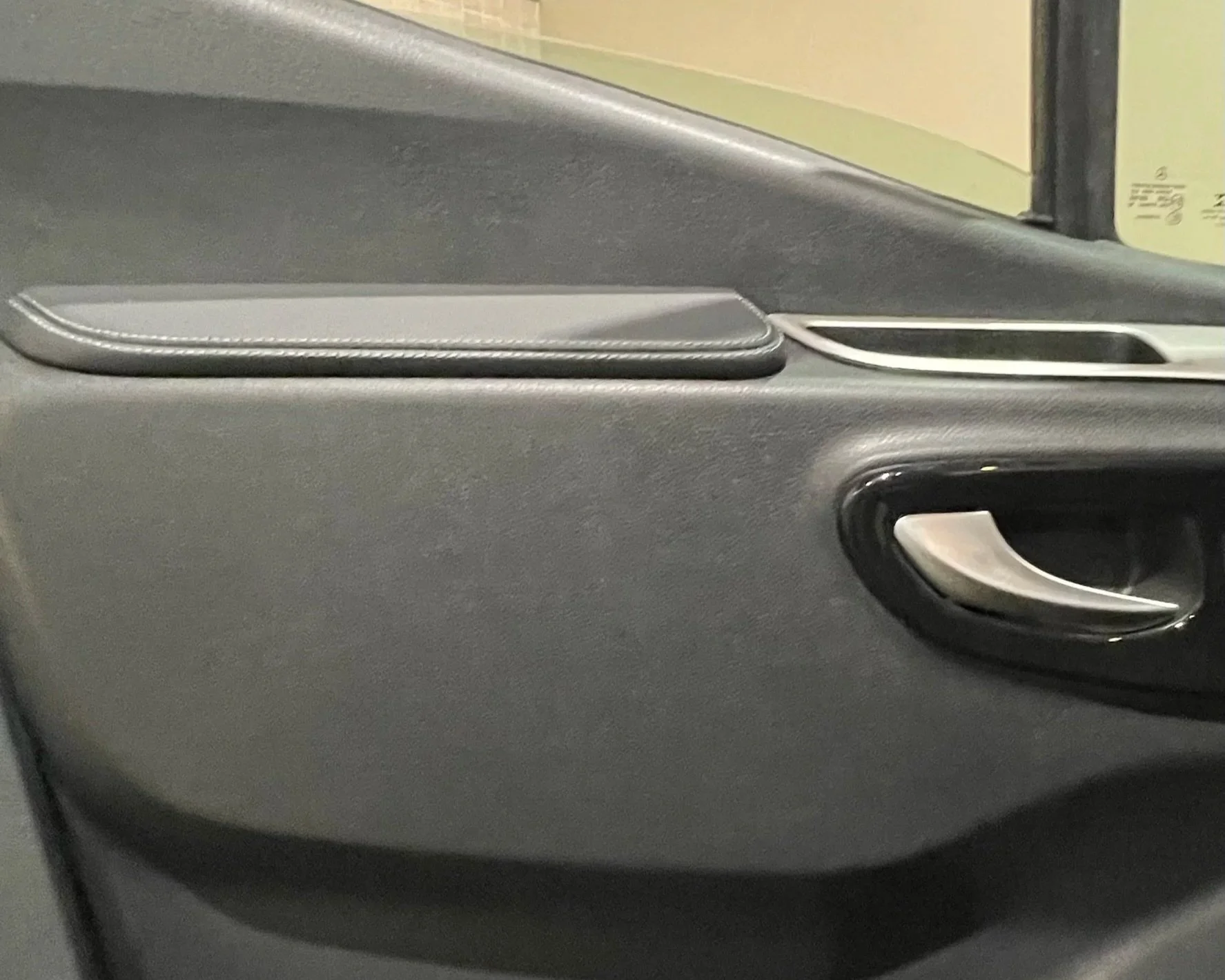 Close-up of a car's interior door panel, showing a door handle, a small storage compartment, and a padded armrest with white stitching.