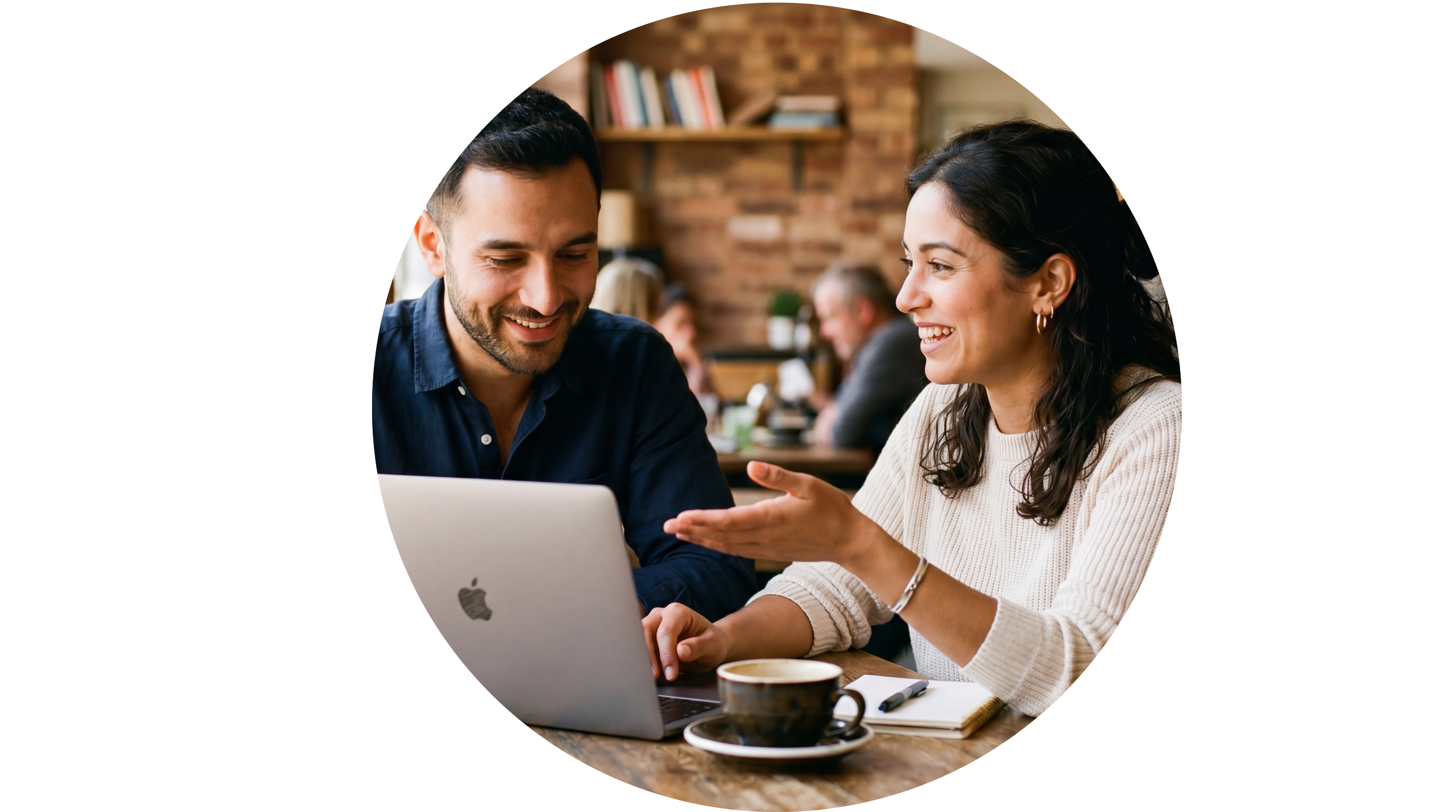 Two people, a man and a woman, smiling and talking while looking at a laptop screen in a cozy cafe setting.