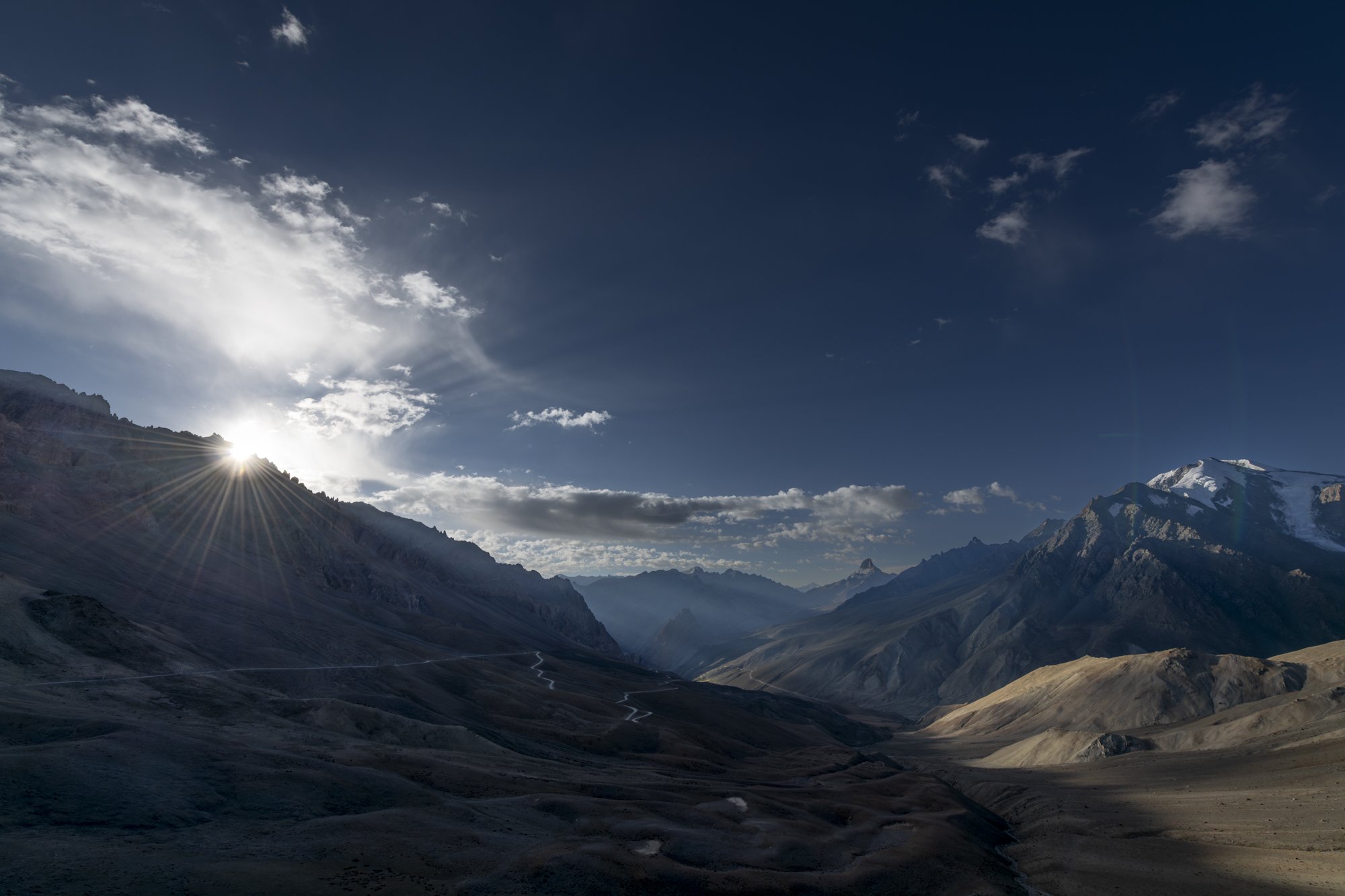 Sonne bricht über dem Singey La, darunter die Serpentinen der Passstrasse, Ladakh