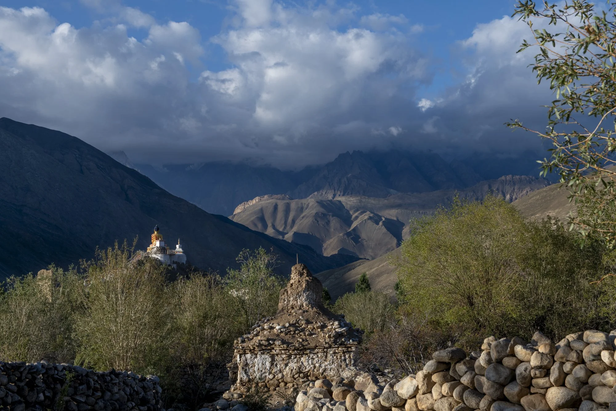 Chörten und Steinmauern in Hemis Shukpachen, dahinter ein vergoldeter Chörten im Licht