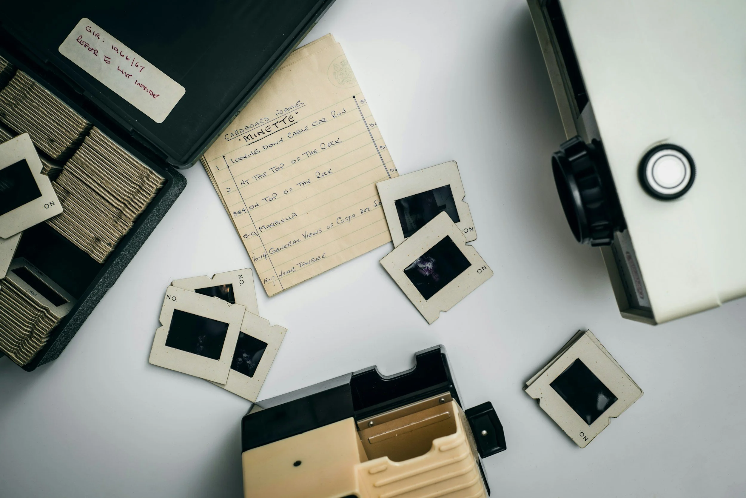 Vintage instant camera with several developed photographs, a yellow note with handwritten instructions, and an unopened film box on a white surface.