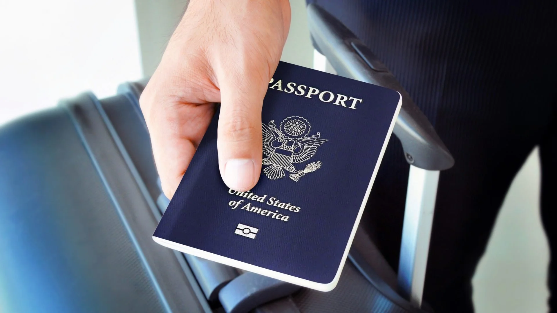 Hand holding a United States passport at an airport, with an airplane seat in the background.