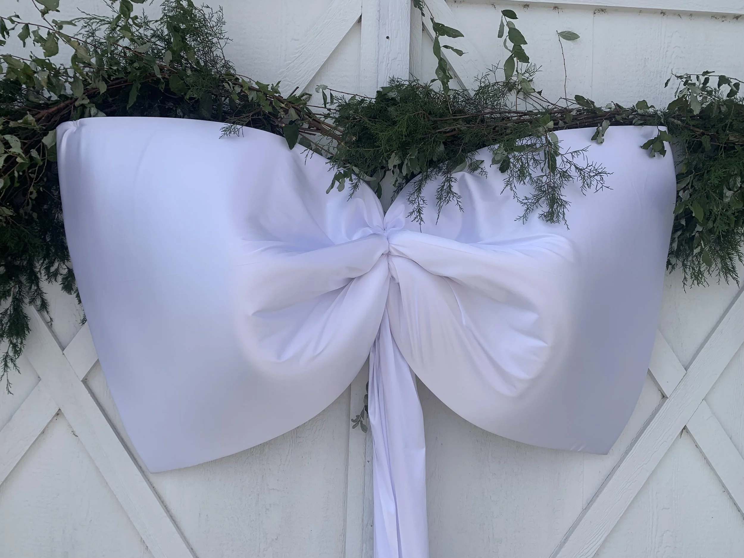 Decorative white bow with greenery on a white fence.