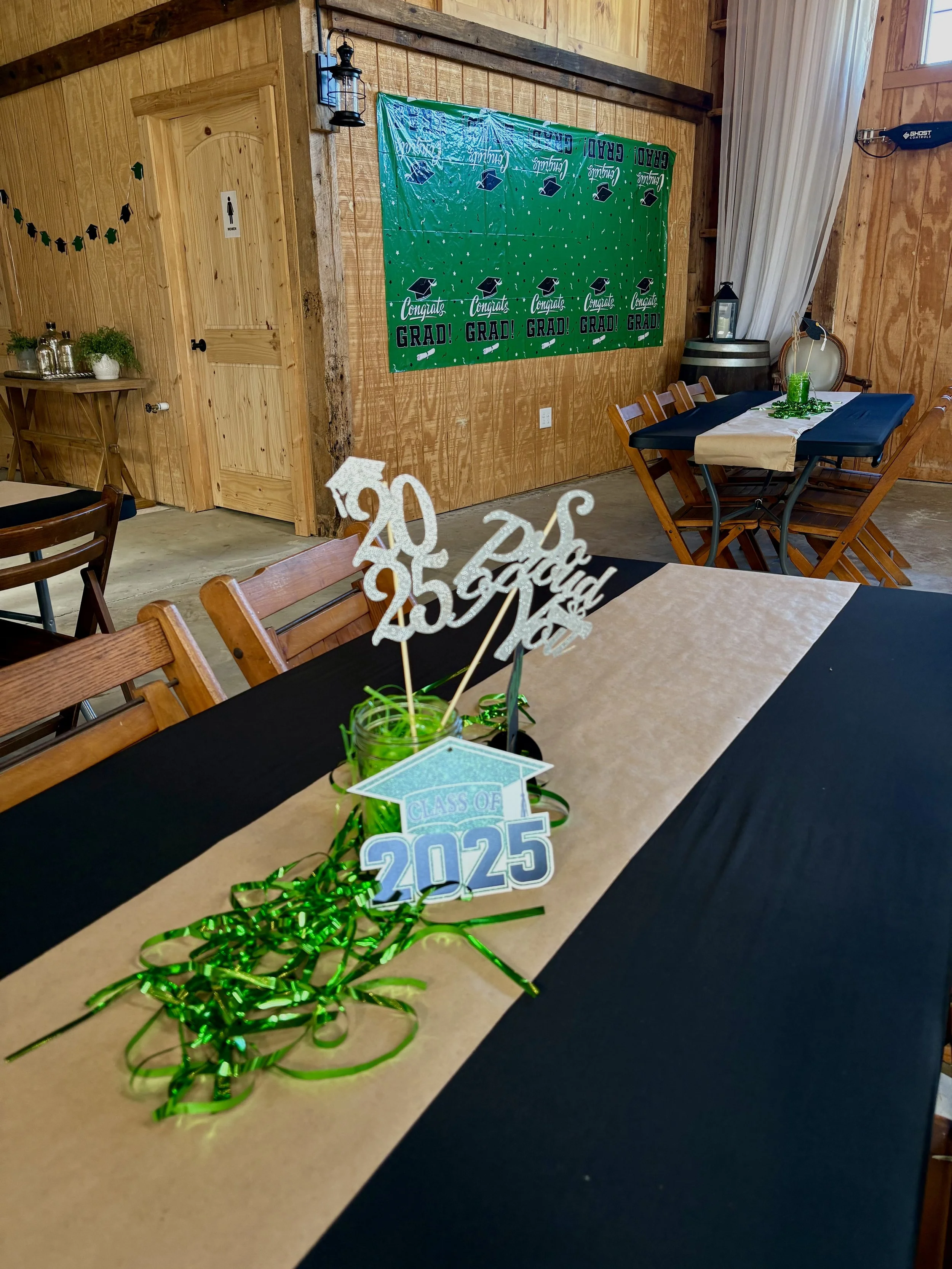 Decorated graduation celebration table with a 'Class of 2025' sign, green ribbon, and 'Congrats Grad' banners on the wall.