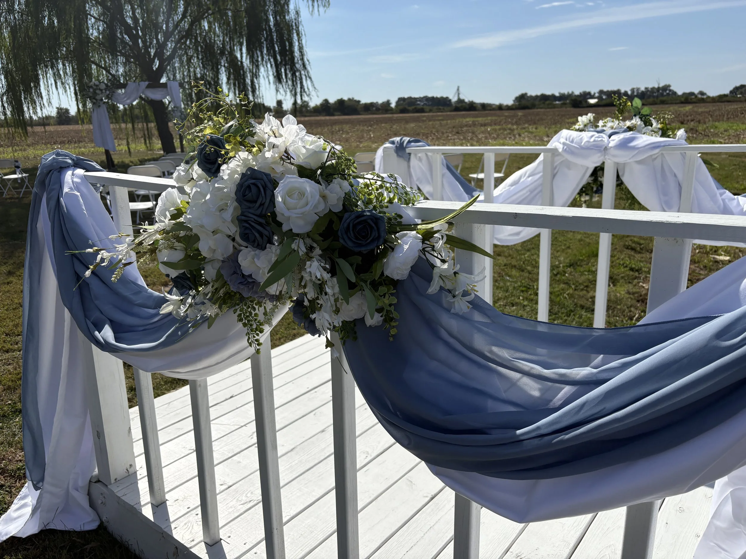 Decorated outdoor wedding gazebo with white and blue drapes and floral arrangements including white and blue roses