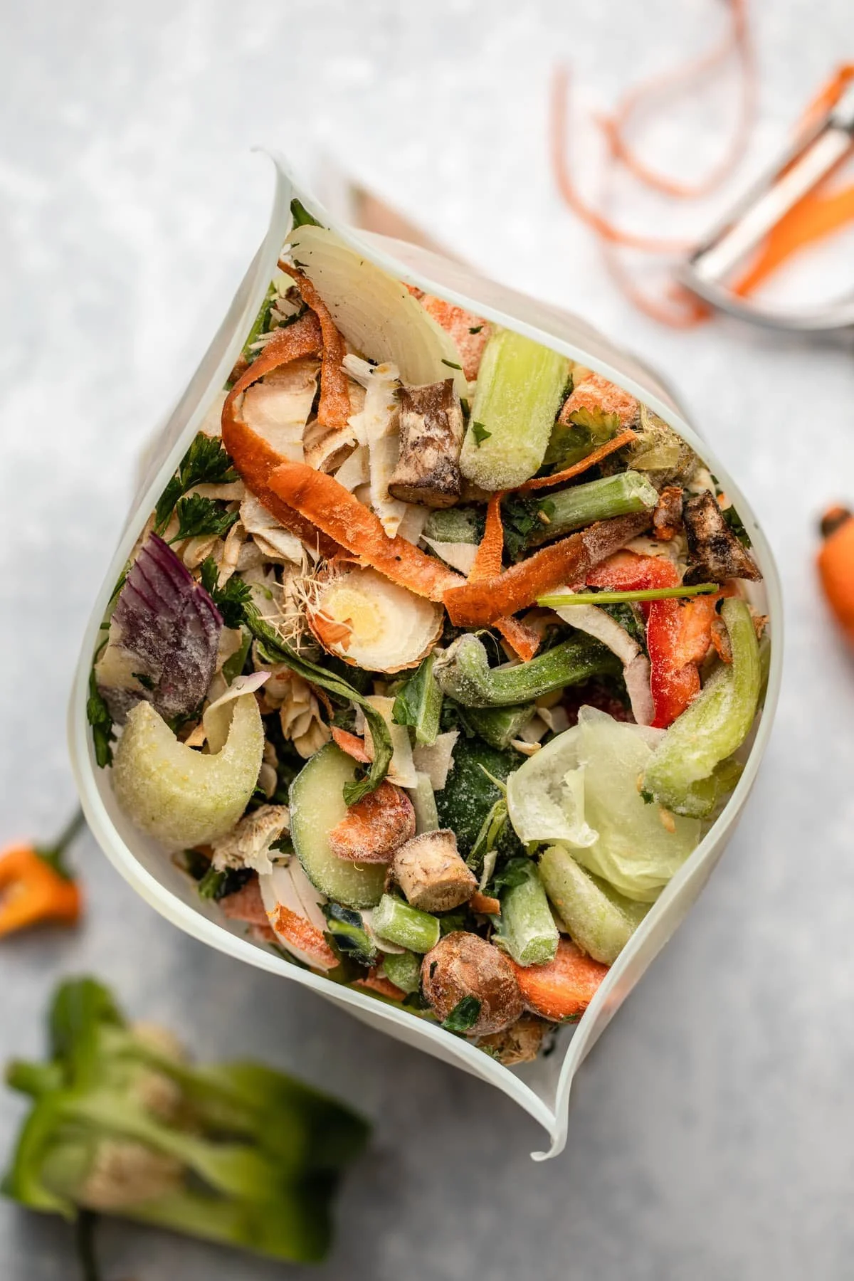 A close-up view of a container filled with a variety of chopped vegetables, including carrots, cucumbers, celery, and leafy greens, with some herbs and seasoning.