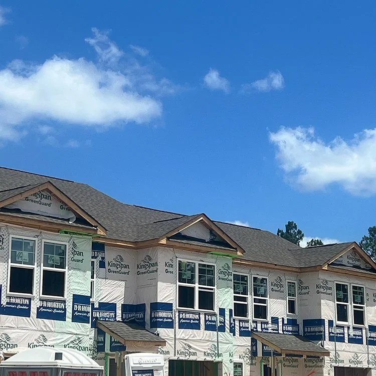 Partially constructed residential building with roof, windows installed, and wrapped in Kingspan GreenGuard underlayment, under a blue sky with clouds.
