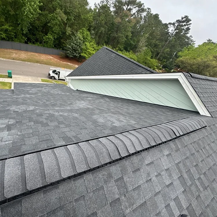 View of a residential roof with asphalt shingles, featuring multiple roof lines and trees in the background.