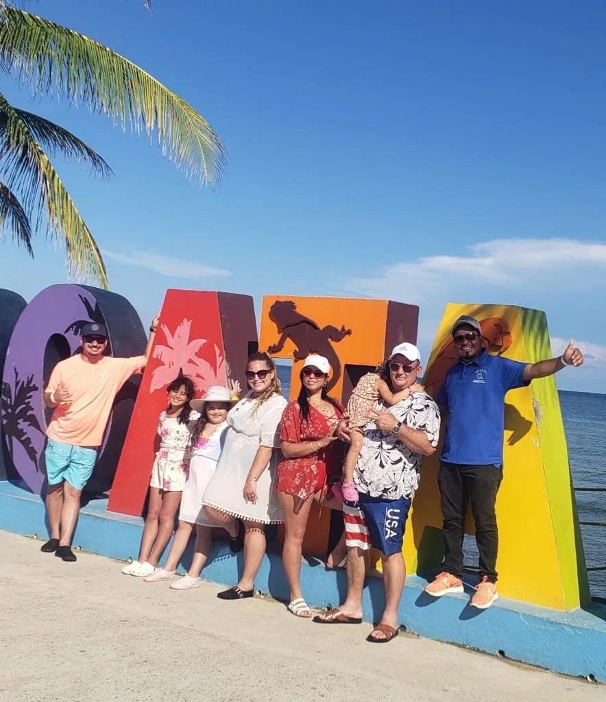 A happy group at the colorful DREAM sign on a Roatan beach