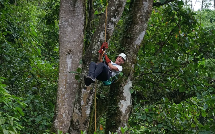 A guest smiling in a harness while zip-lining through the forest