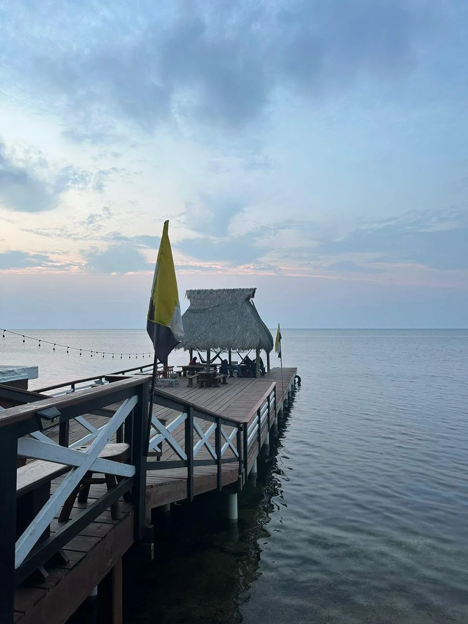 A dock with a thatched hut and umbrellas at sunset