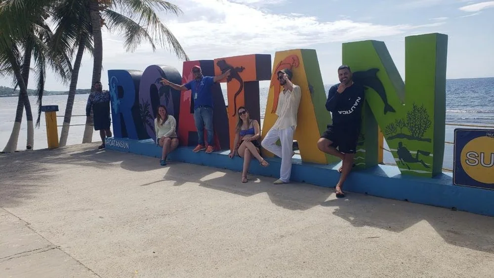 A group posing in front of the colorful ROATAN letters by the beach