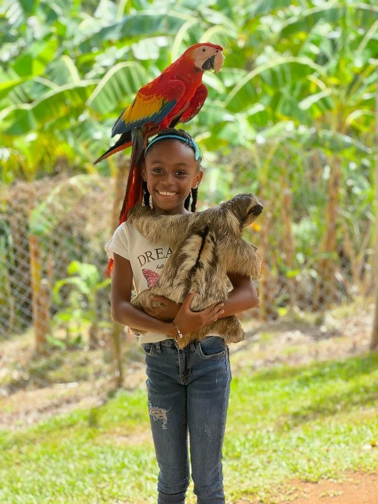 A girl holding a capybara with a parrot perched on her head