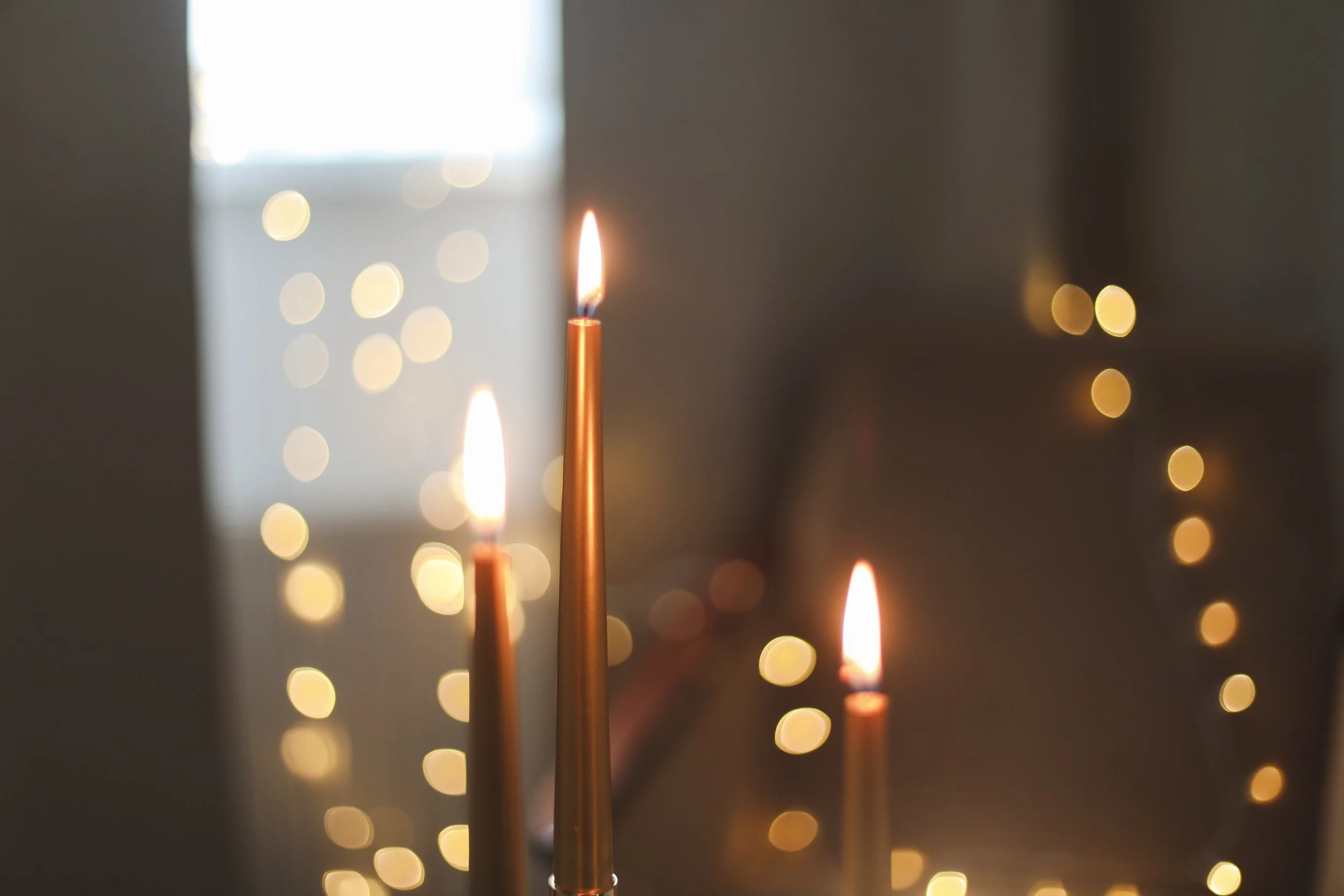 Three lit candles with a background of blurred warm yellow fairy lights.
