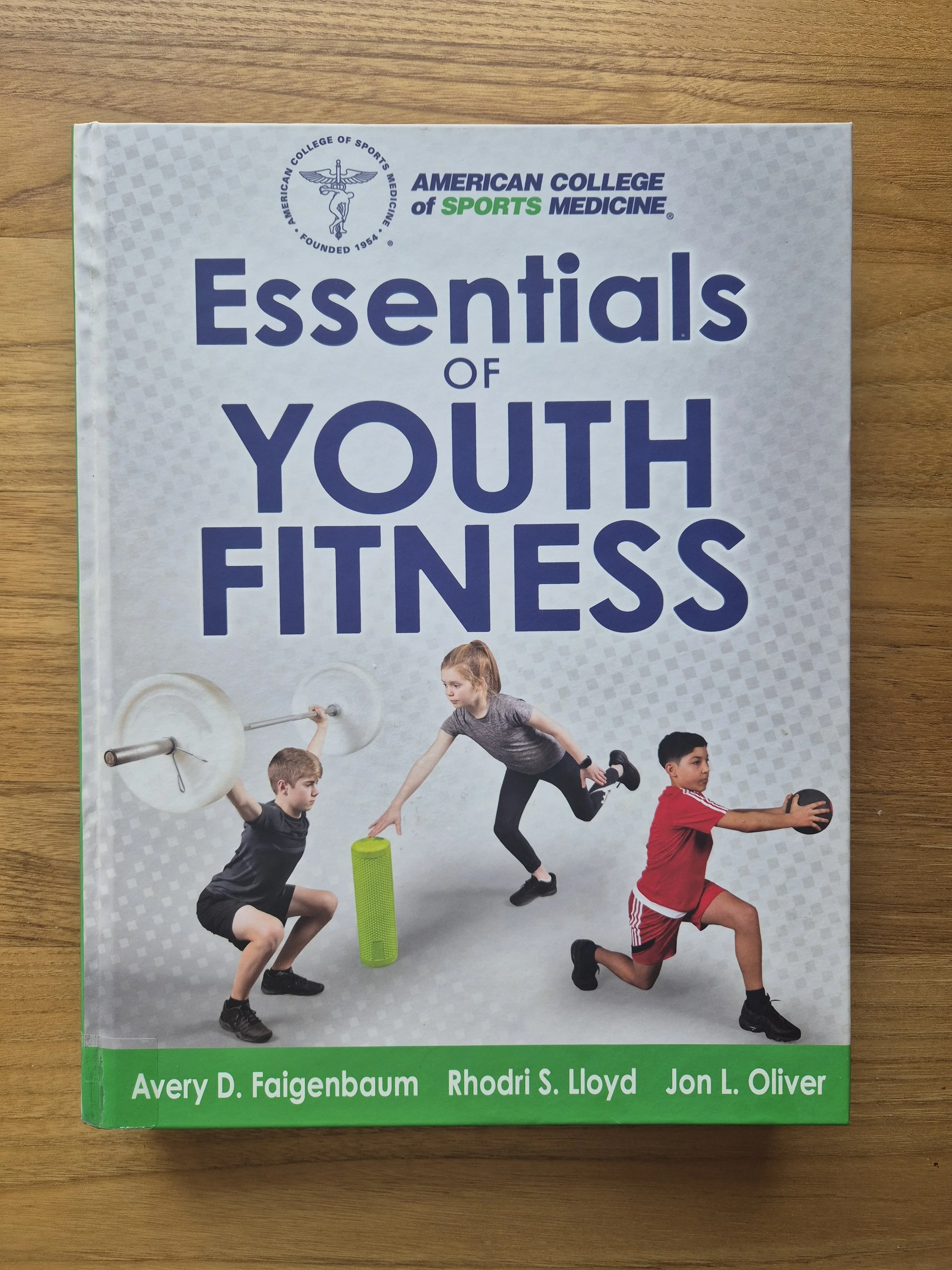 Book titled "Essentials of Youth Fitness" with a group of children exercising with weights, foam roller, and medicine ball on the cover.