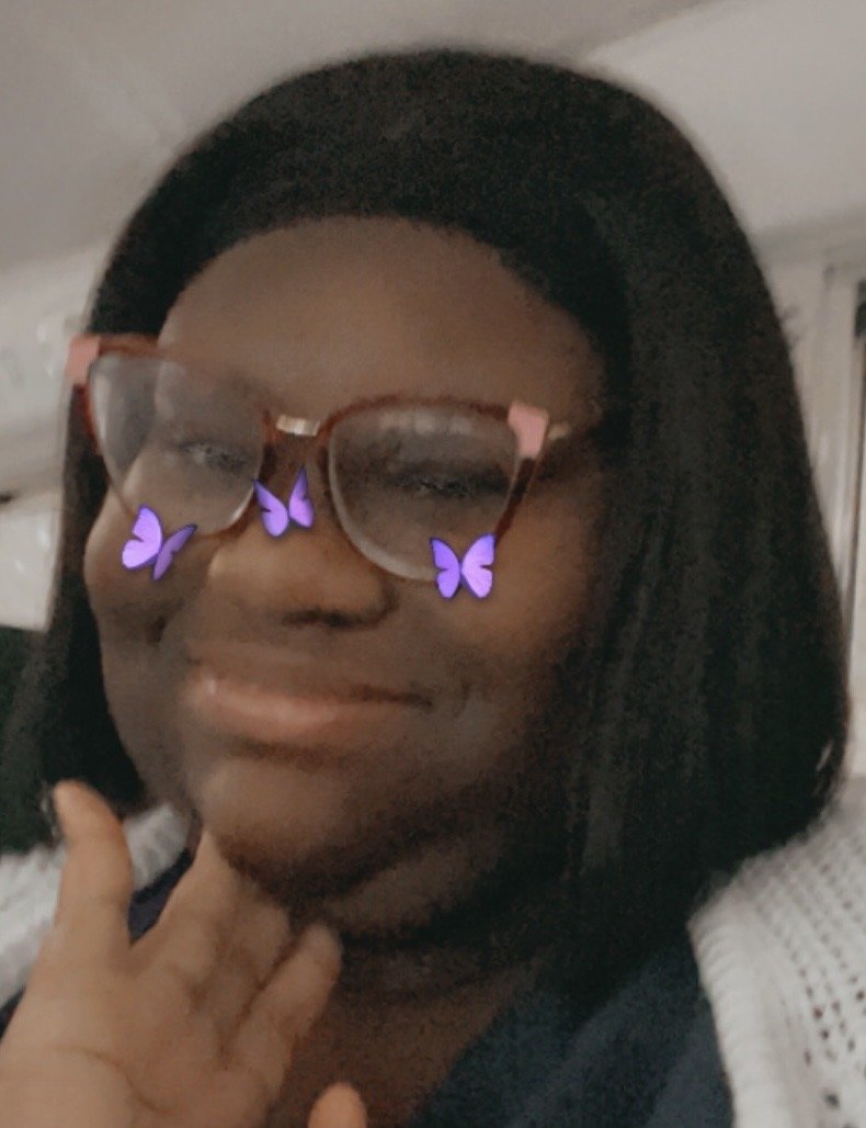 Person wearing glasses with a filter of purple butterflies on their face, smiling indoors.
