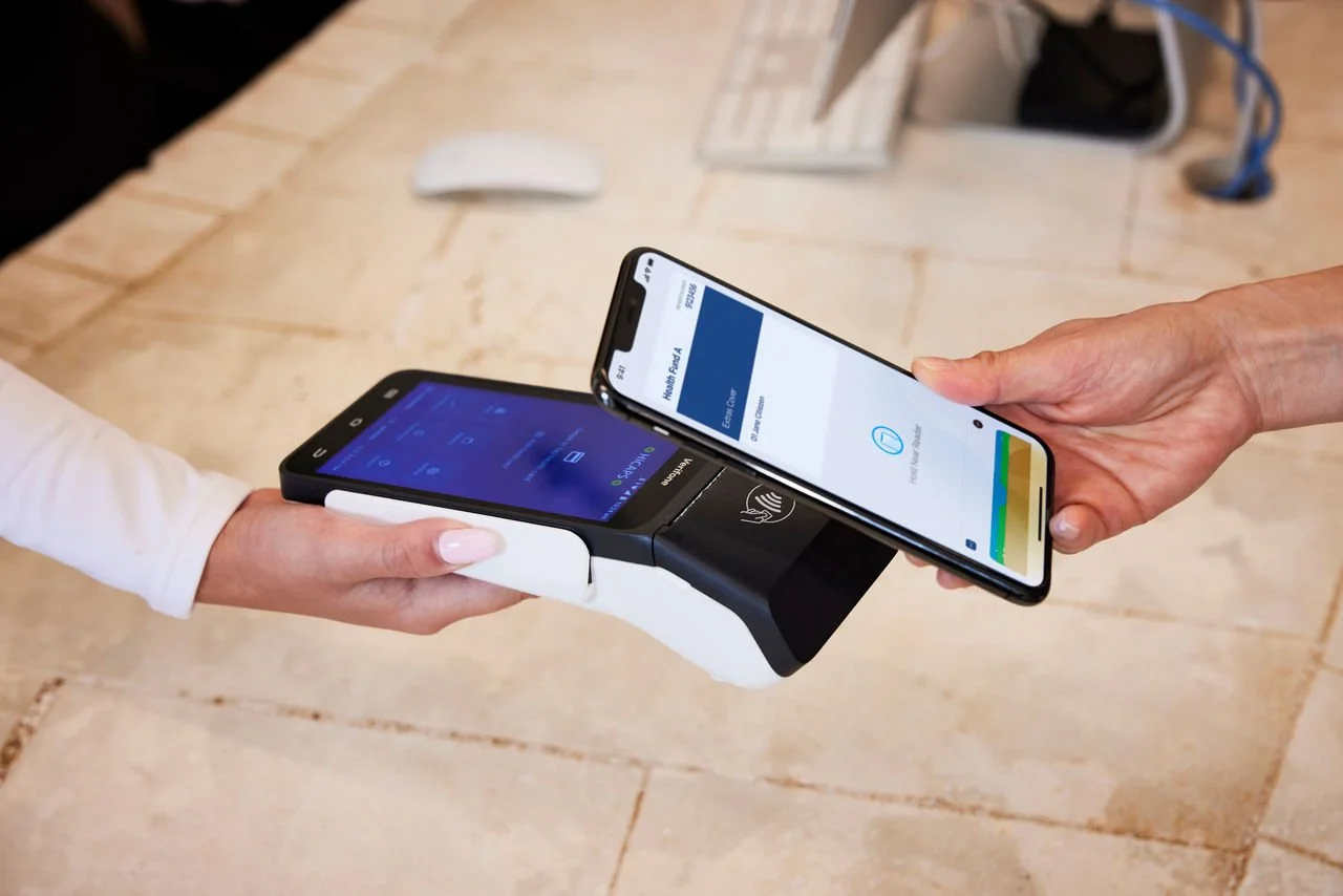 Person using a smartphone for a contactless payment transaction with a card reader on a wooden table.