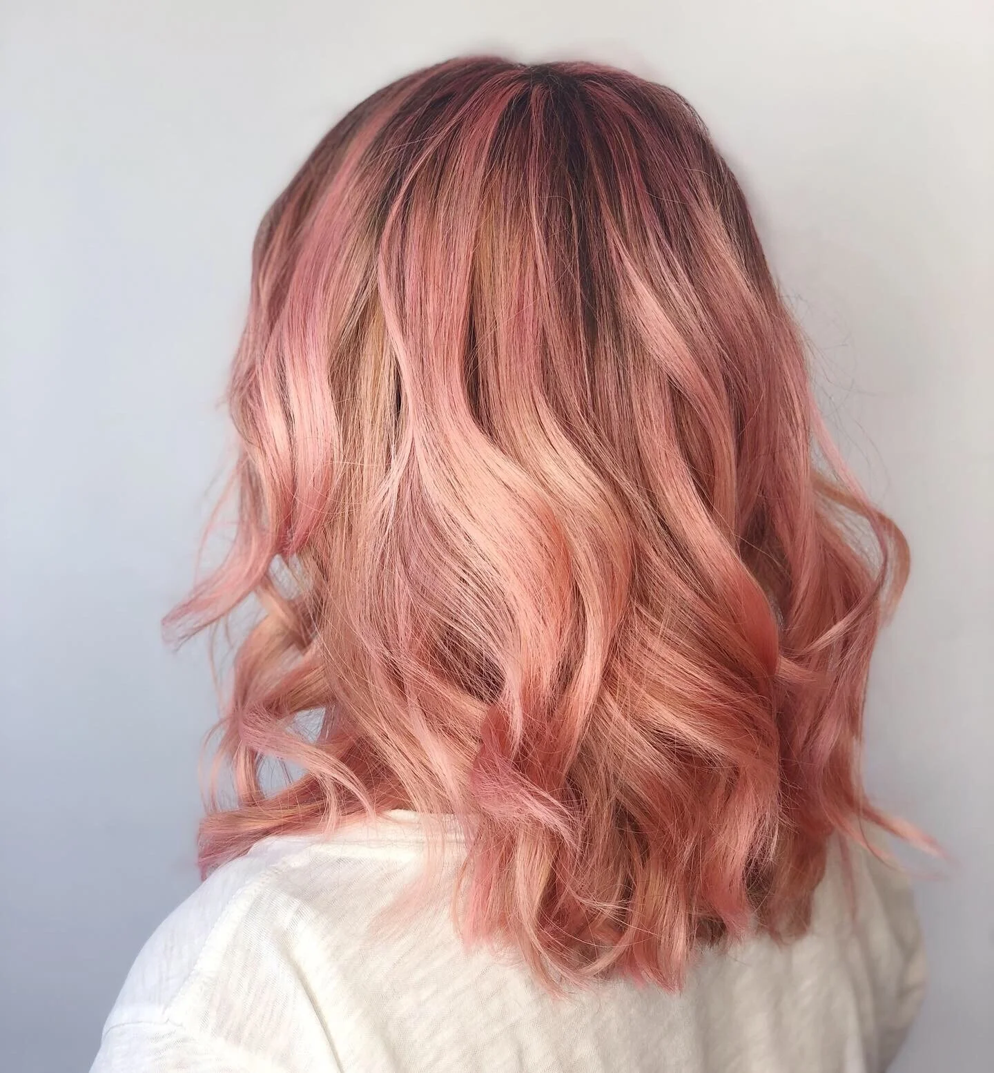 Back view of a woman with shoulder-length wavy hair dyed in shades of pink, orange, and blonde.