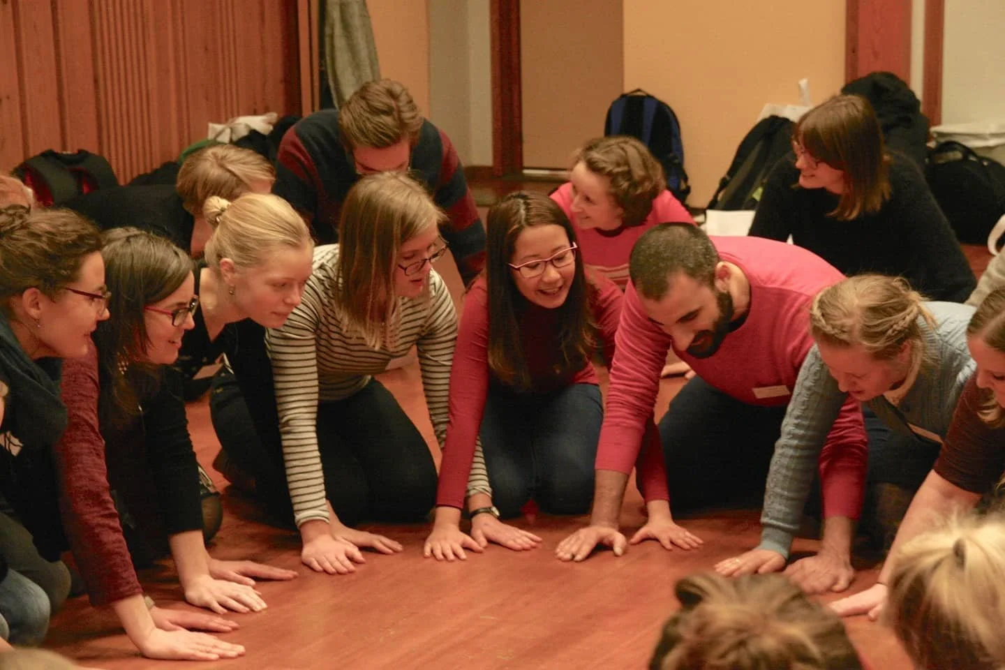 Group of people sitting and crouching on the floor, smiling and engaging in a team-building activity or game.