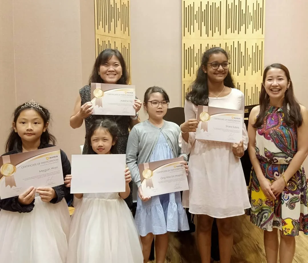 A group of seven women and girls standing indoors, with some holding certificates of participation. They are smiling, and the women are dressed in colorful clothes.