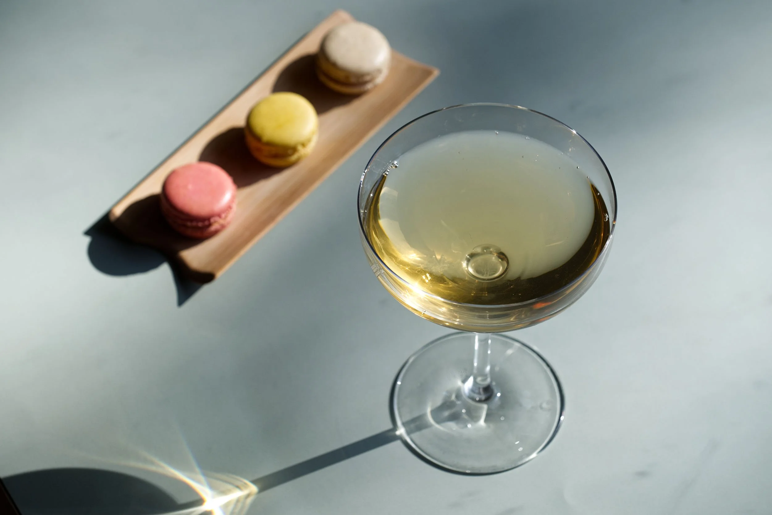 Glass med te og en tretasjers tallerken med macarons i rosa, gult og beige