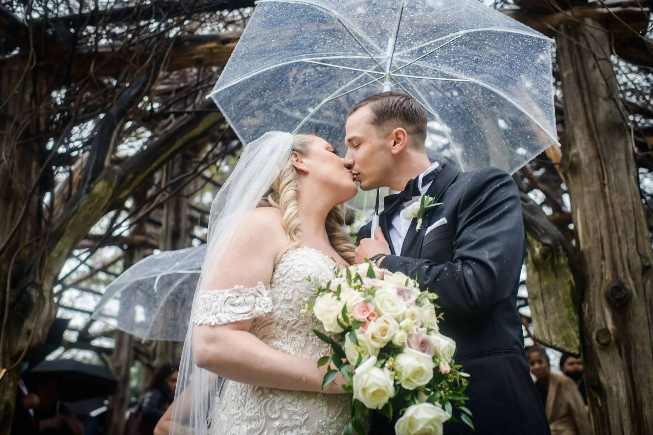 Bride-and-groom-kissing-under-a-clear umbrella-with-a-bridal-bouquet-in-central-park.jpg