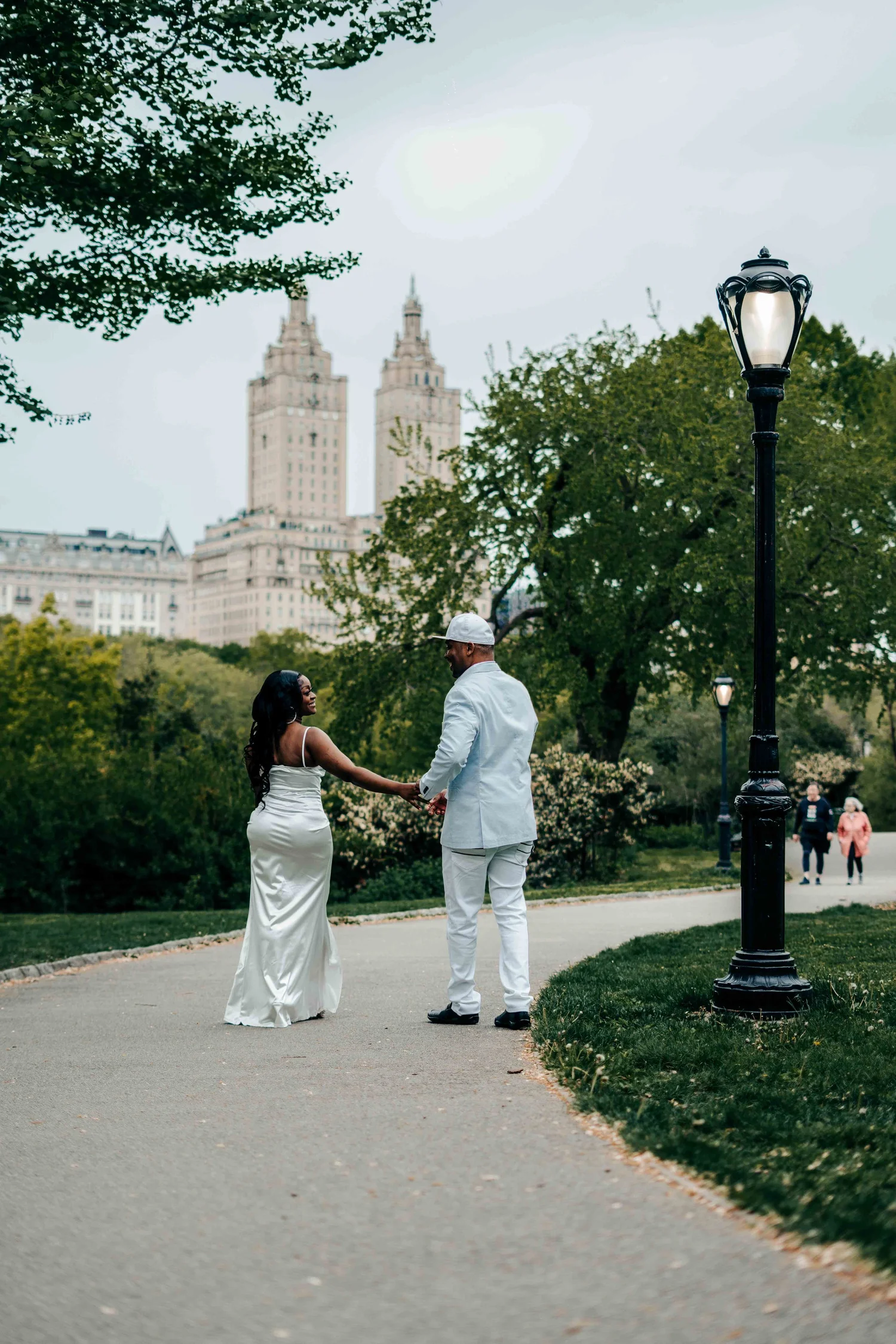 Bride and groom walking hand in hand in Central Park with city buildings behind them