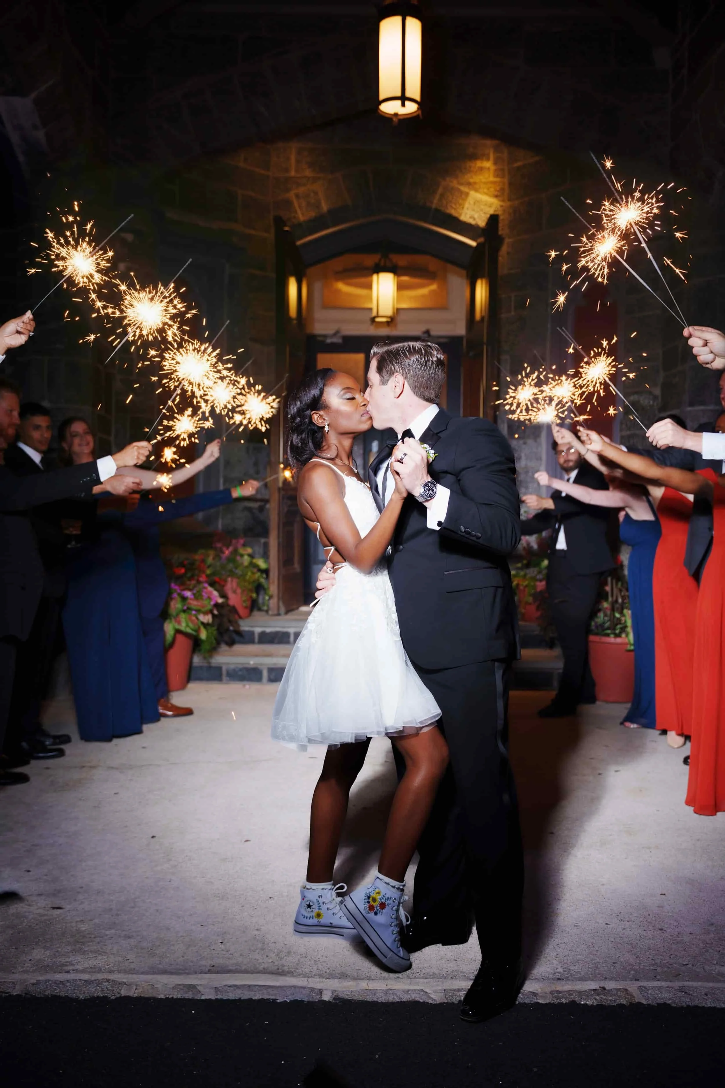 A newlywed couple sharing a dance and kiss, surrounded by guests holding sparklers at night outside Whitby Castle