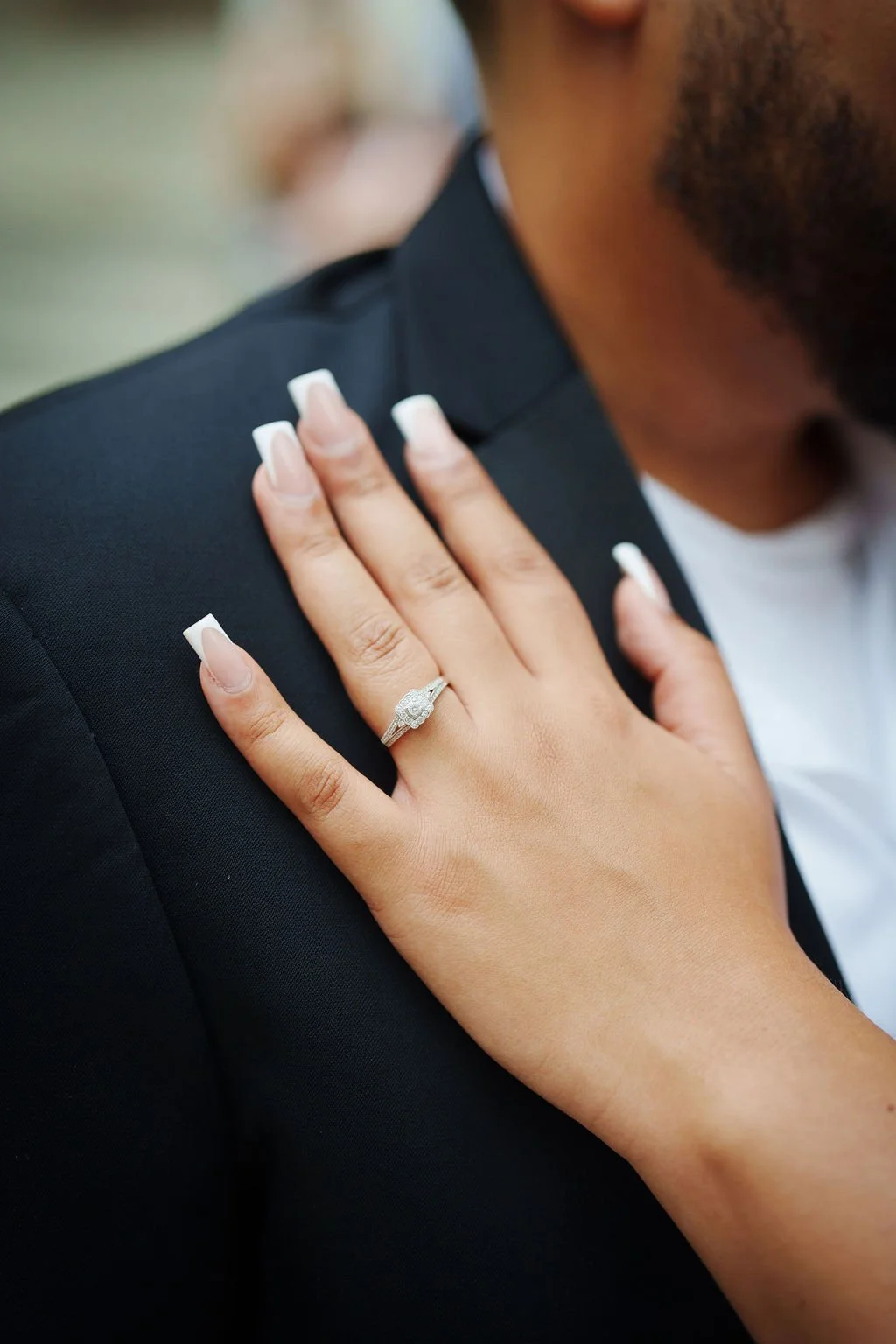 A close-up of a hand with a diamond ring rests on a shoulder after an NYC City Hall wedding, both dressed in formal attire.