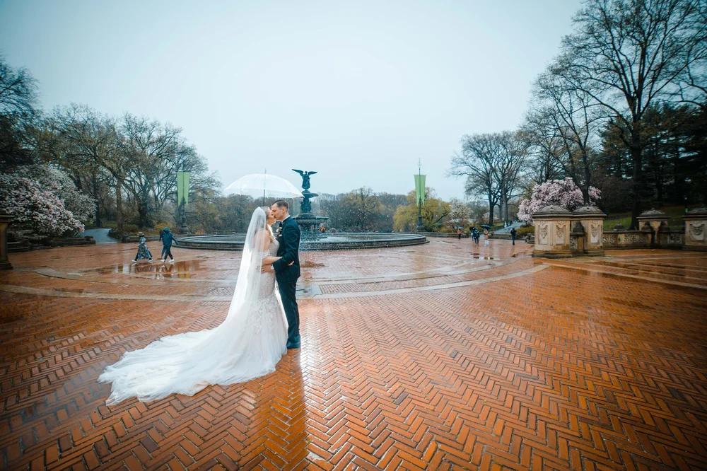 Bride and groom kissing under an umbrella near Bethesda Fountain in Central Park