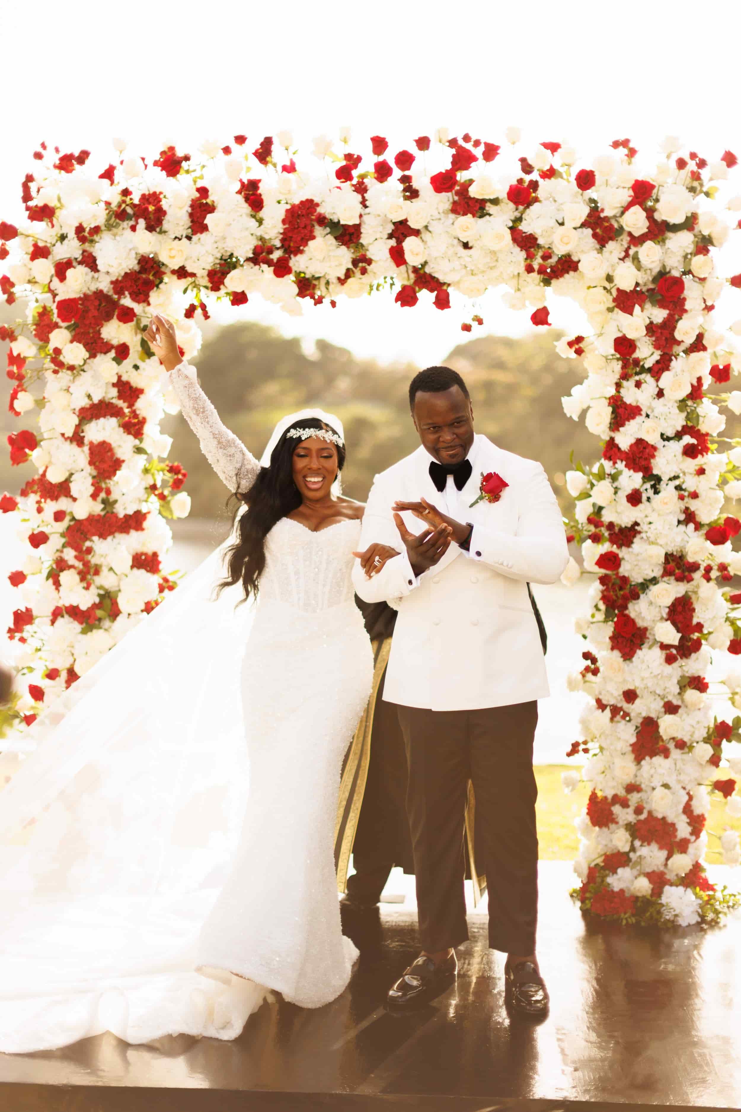 Trident Castle wedding ceremony with bride and groom under red and white floral arch by the ocean