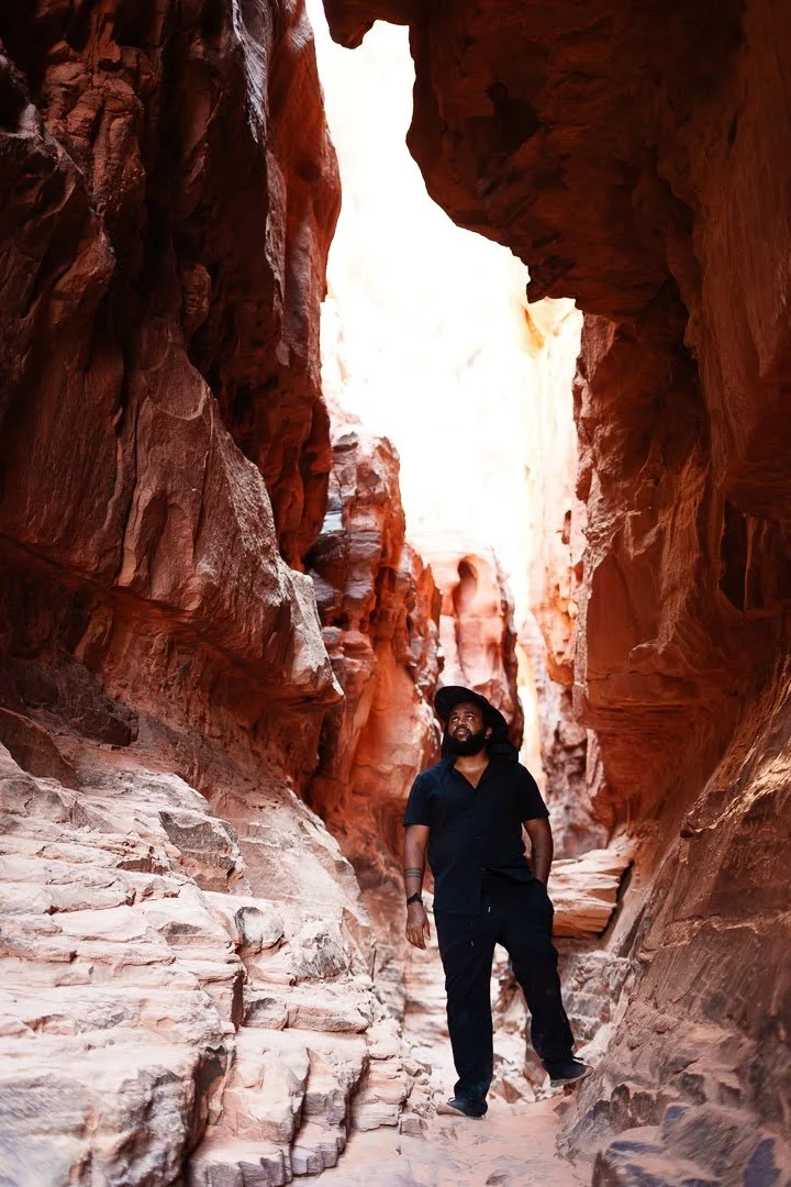 New York City Wedding Videographer Dane Nelson in black clothing and hat standing in a narrow red rock canyon in Jordan.