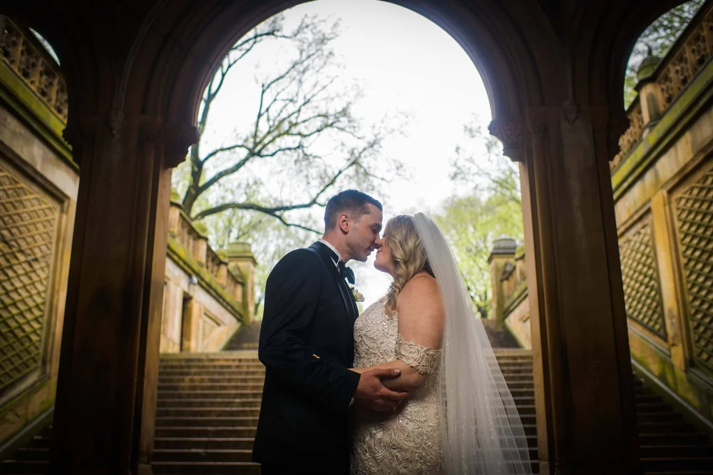 Bride and groom kissing under an ornate archway at Bethesda Terrace
