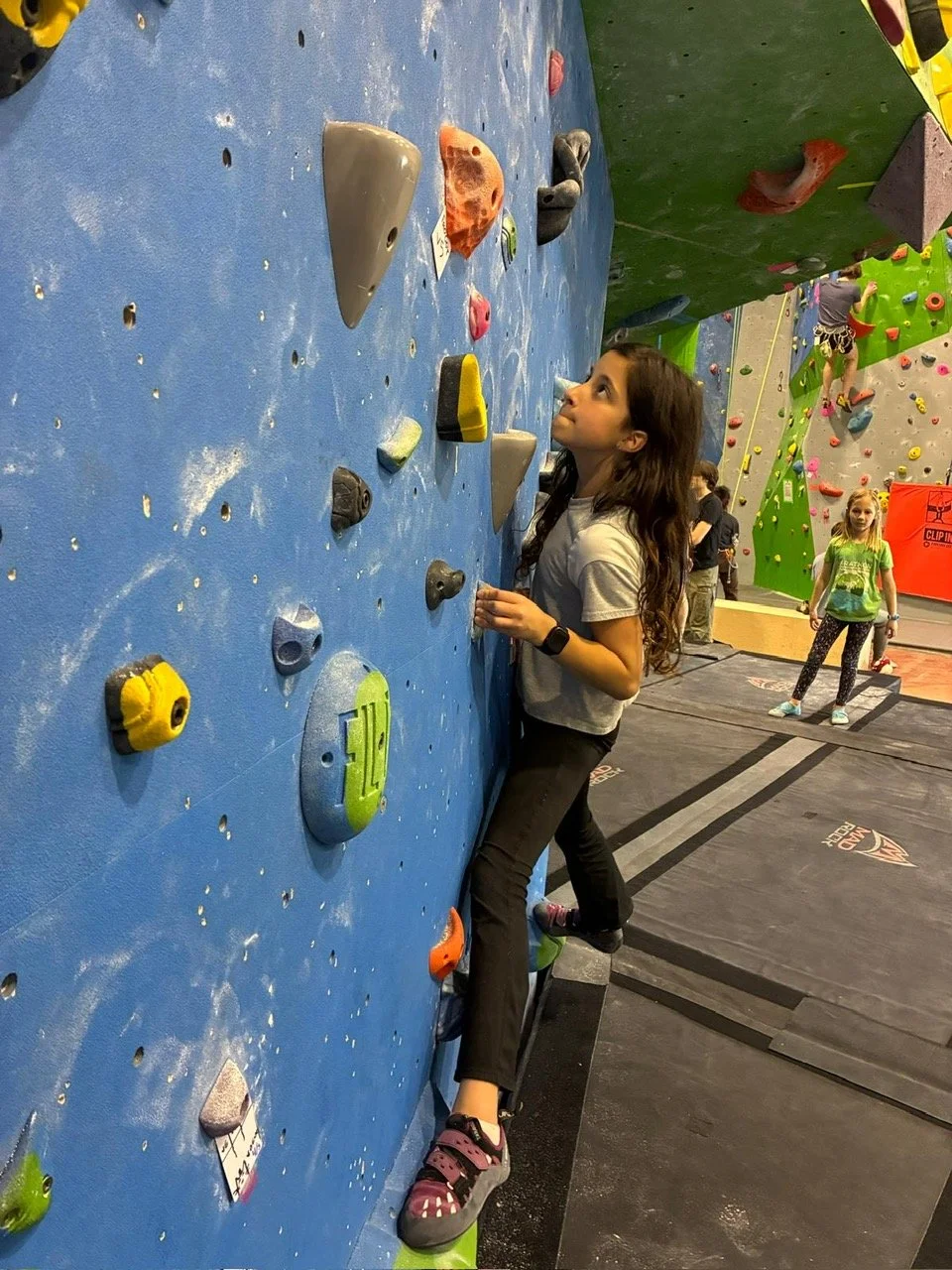 A woman climbing an indoor rock wall while being belayed by a man.