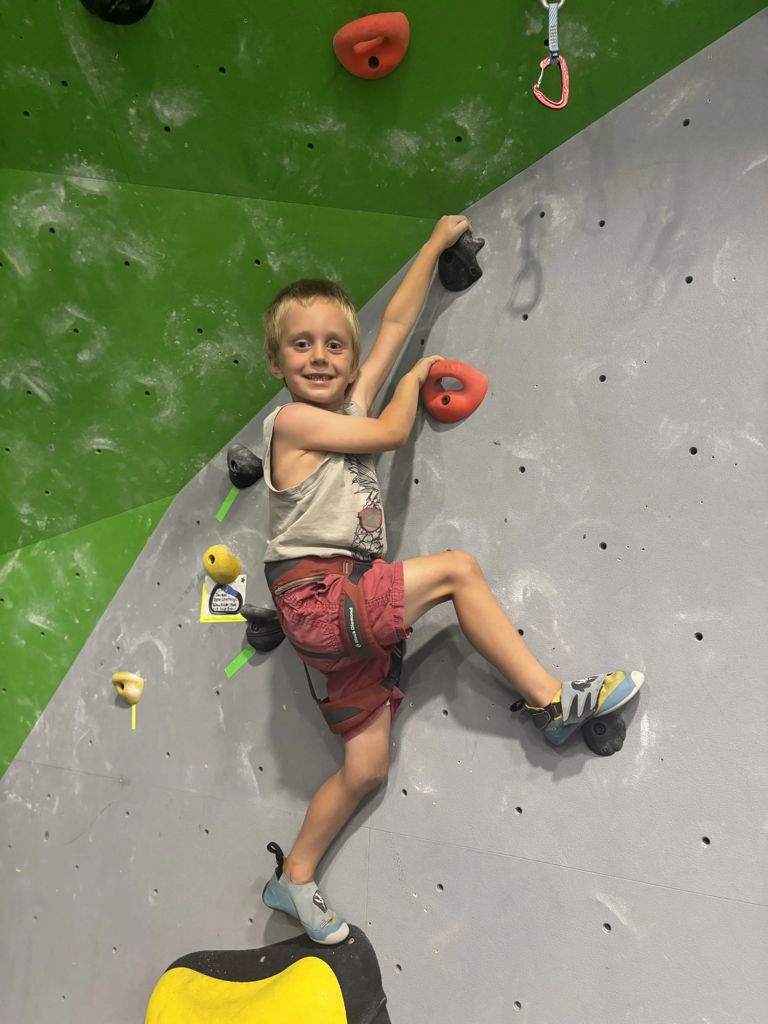 People watching individuals climbing an indoor rock climbing wall with colorful holds in a gym.