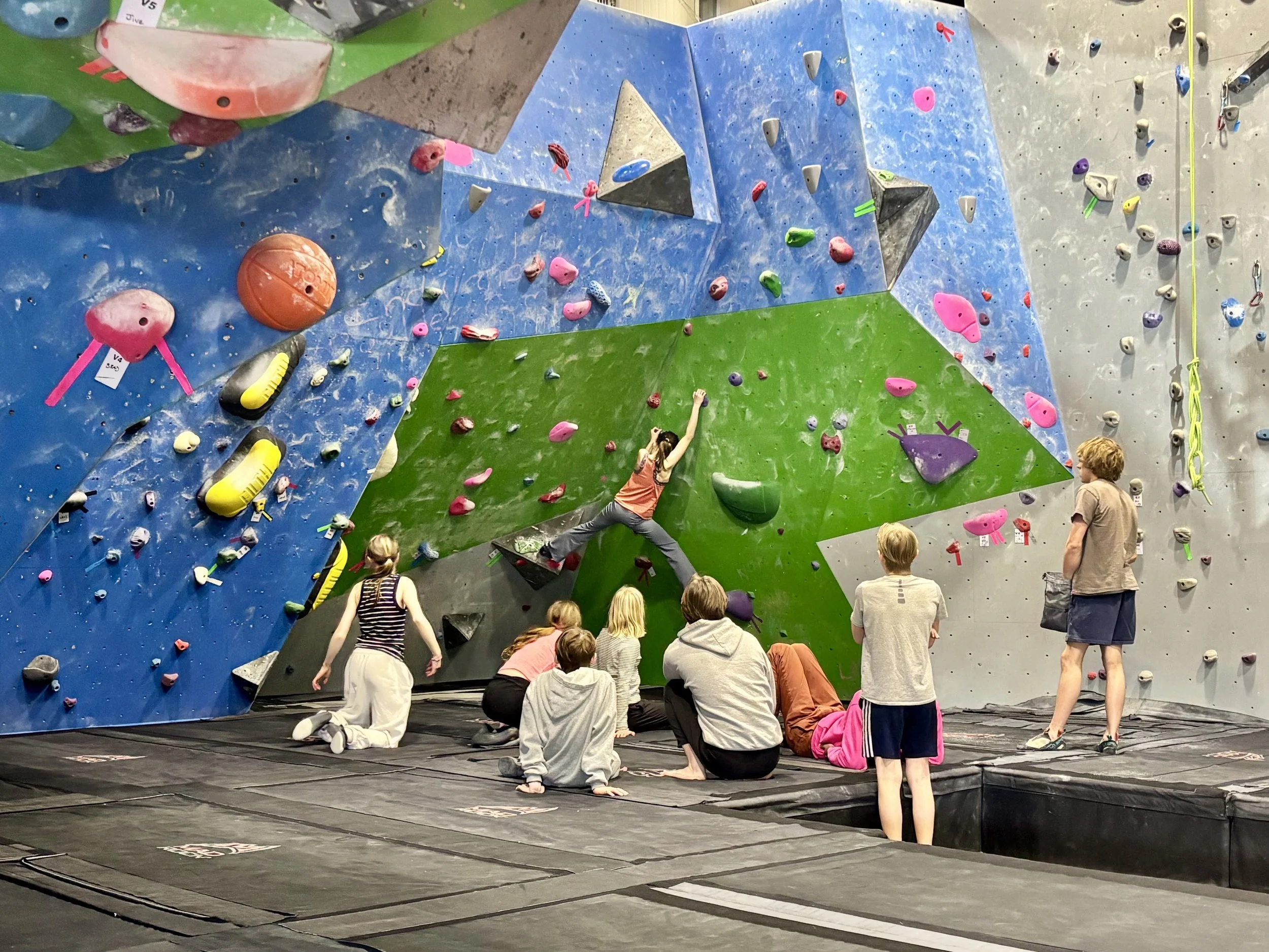 A woman climbing an indoor rock wall while being belayed by a man.