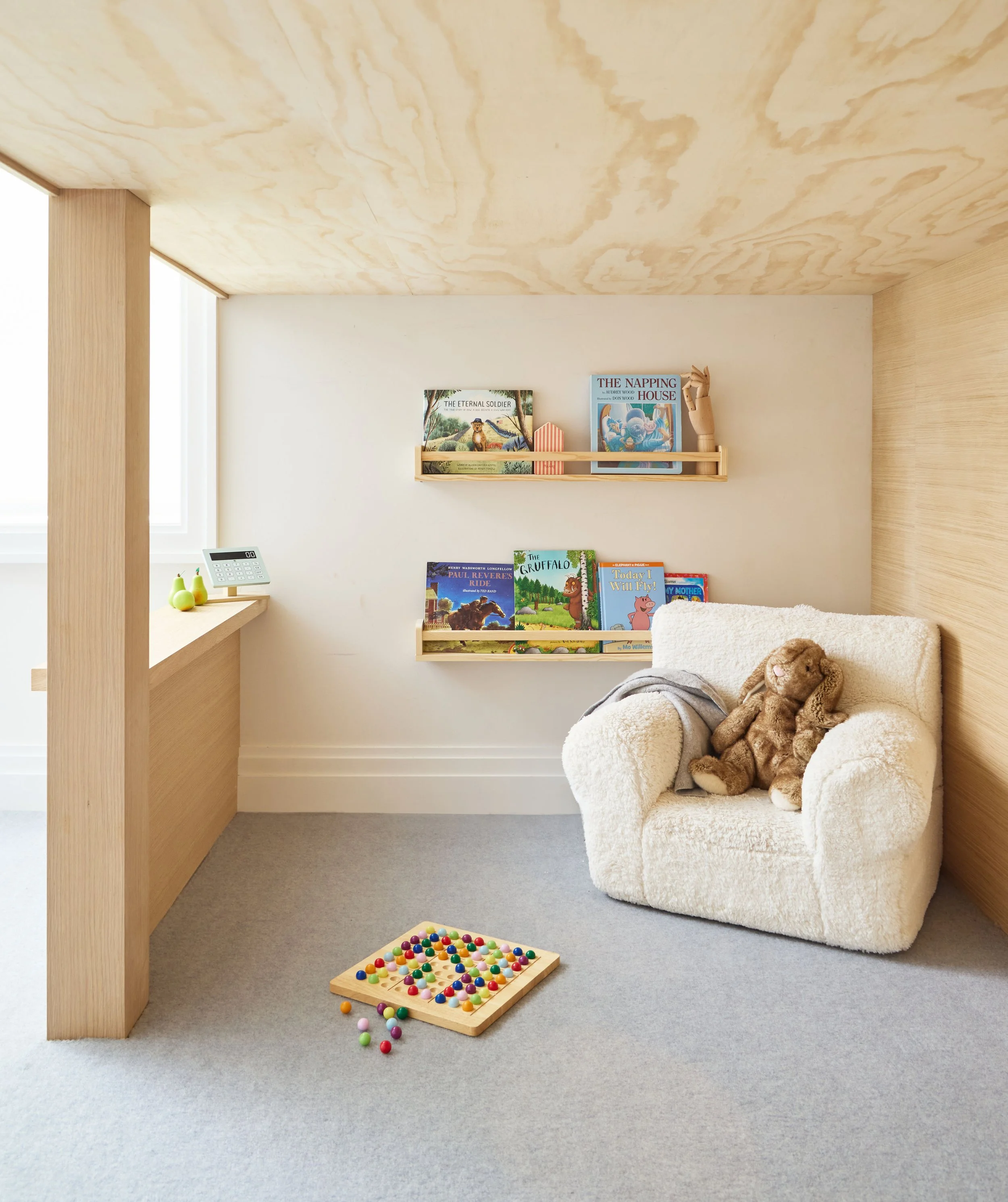 Cozy kids' reading nook with forward-facing bookshelves and child-sized chair inside a custom play fort