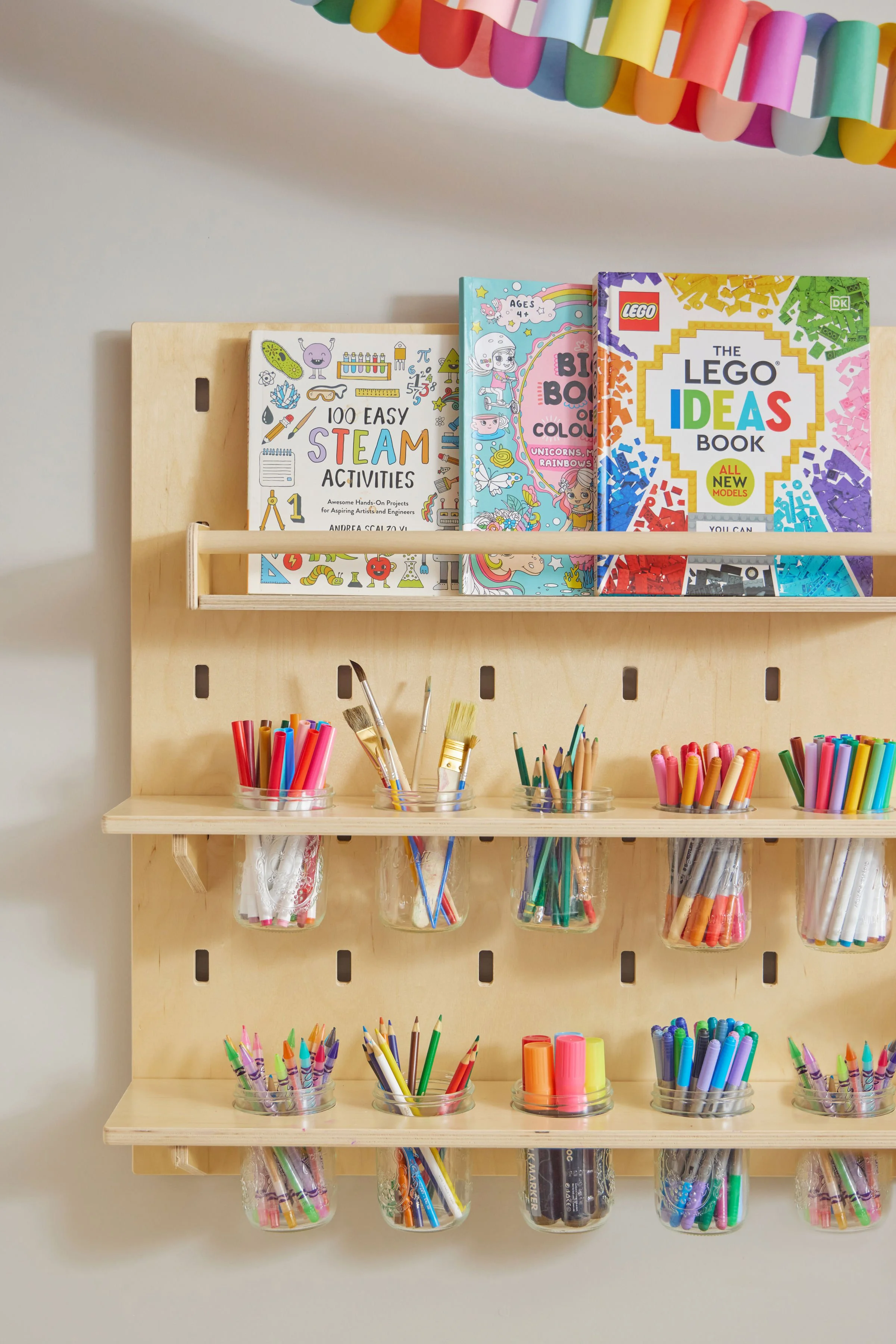 Wooden pegboard art supply wall with book ledges and jars of colored pencils and markers in a kids' playroom
