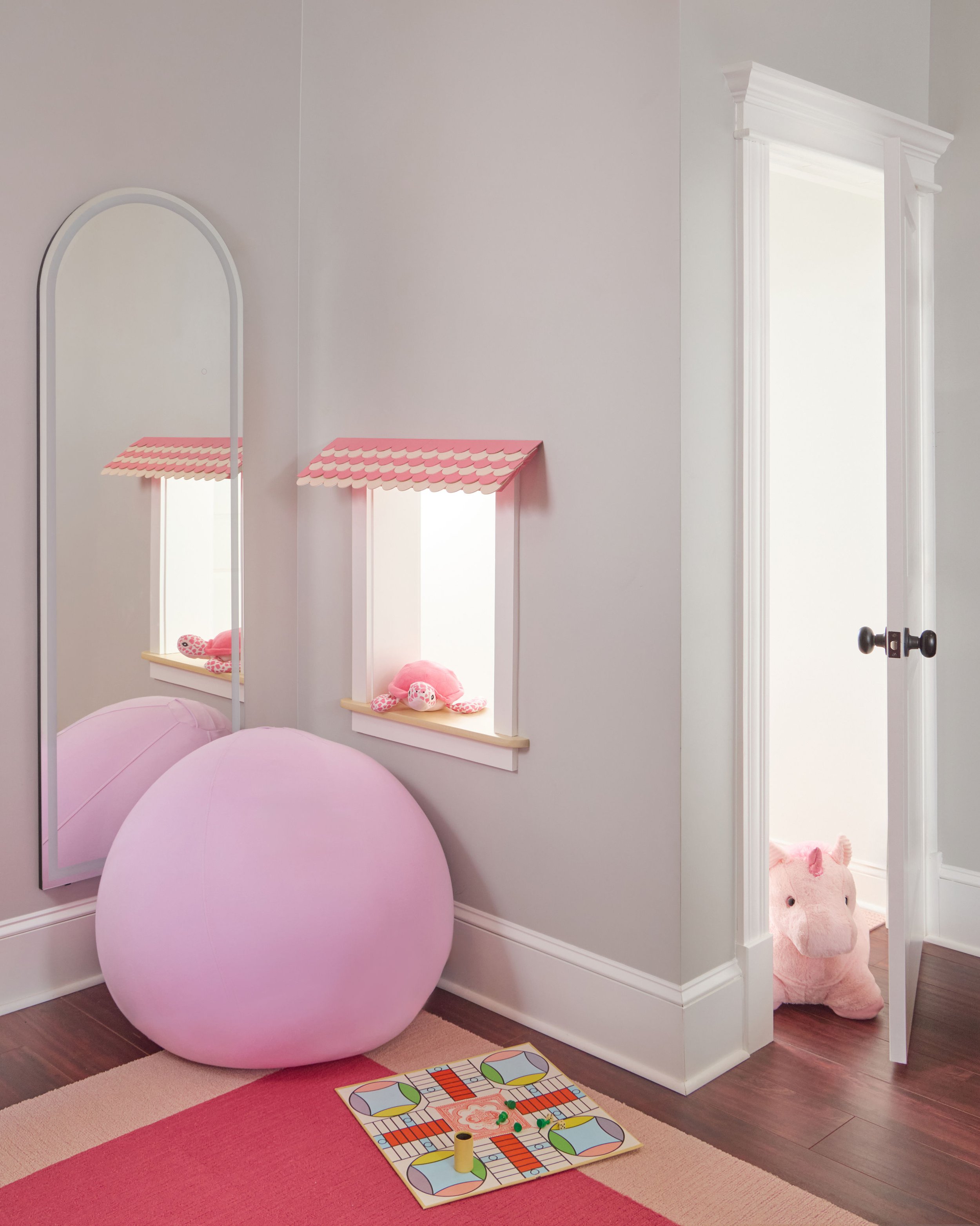 Built-in playhouse windows with pink striped awnings, arched mirror, and pink ball chair in a girls' playroom